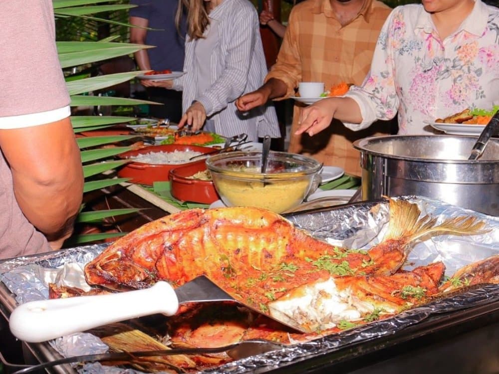 Frisch aus dem Fluss auf den Tisch – gebratener Fisch als Highlight des Dschungel-Buffets. Ein ganzer gebratener Fisch mit Kräutern auf einer Folienschale bei einem Outdoor-Buffet auf einer Brazil-Amazon-Dschungeltour, umgeben von Reis, einer goldenen Sauce und weiteren Gerichten