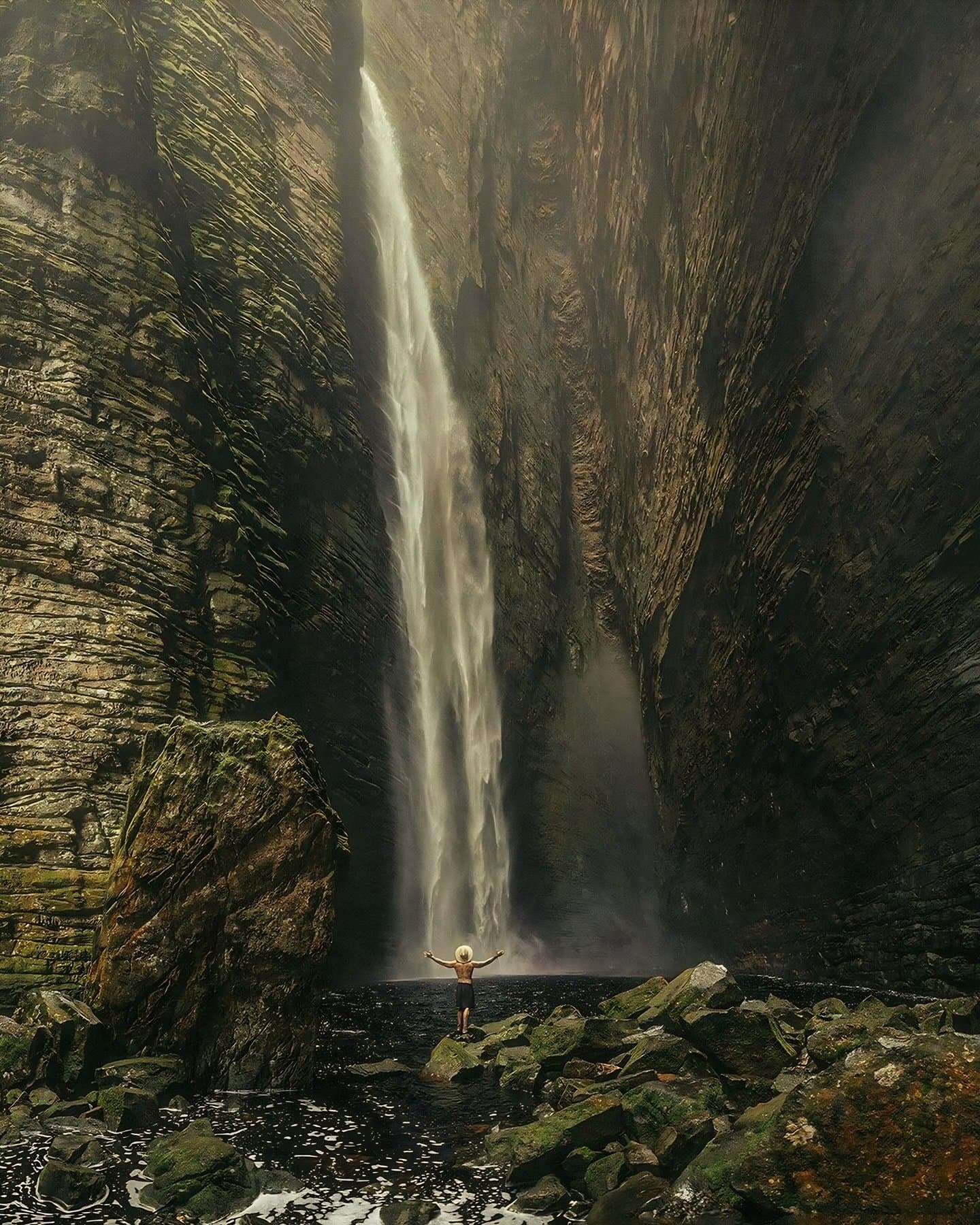 Braços abertos, cabeça no lugar, cachoeira no comando. Um caminhante solitário de braços abertos diante da cachoeira Fumacinha despencando por um cânion estreito de arenito durante uma trilha na Chapada Diamantina
