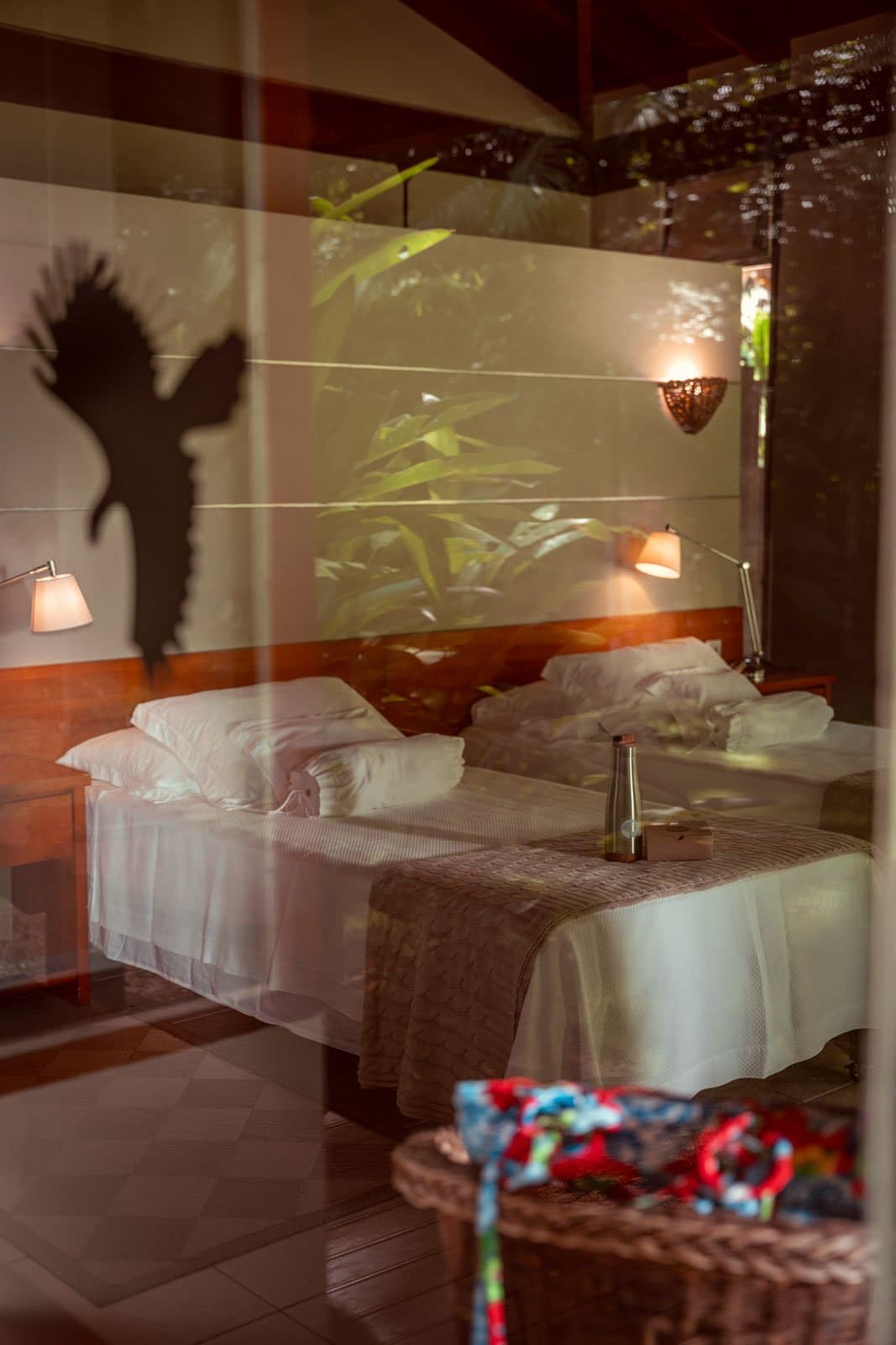Die Natur draußen wirft hier buchstäblich ihren Schatten hinein. Silhouette eines großen Vogels, die auf die Wand eines Doppelzimmers der Cristalino Jungle Lodge fällt, gespiegelt in einer Glasscheibe mit warmem Lampenlicht und tropischem Laub