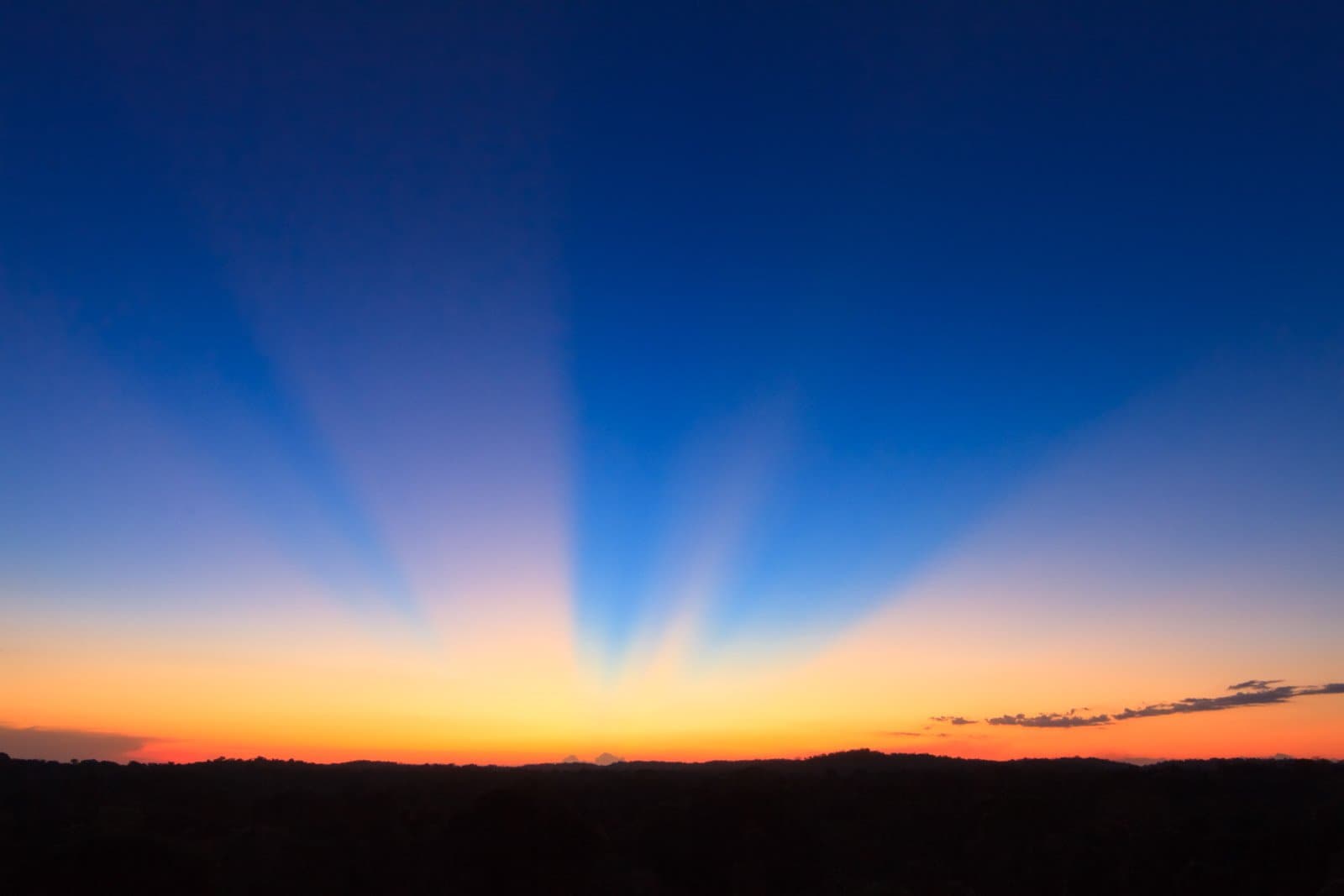 Der Himmel dreht auf, der Wald hält still. Dramatische Krepuskularstrahlen fächern sich über einen tiefblauen Abendhimmel über der dunklen Waldsilhouette des Cristalino Jungle Lodge auf