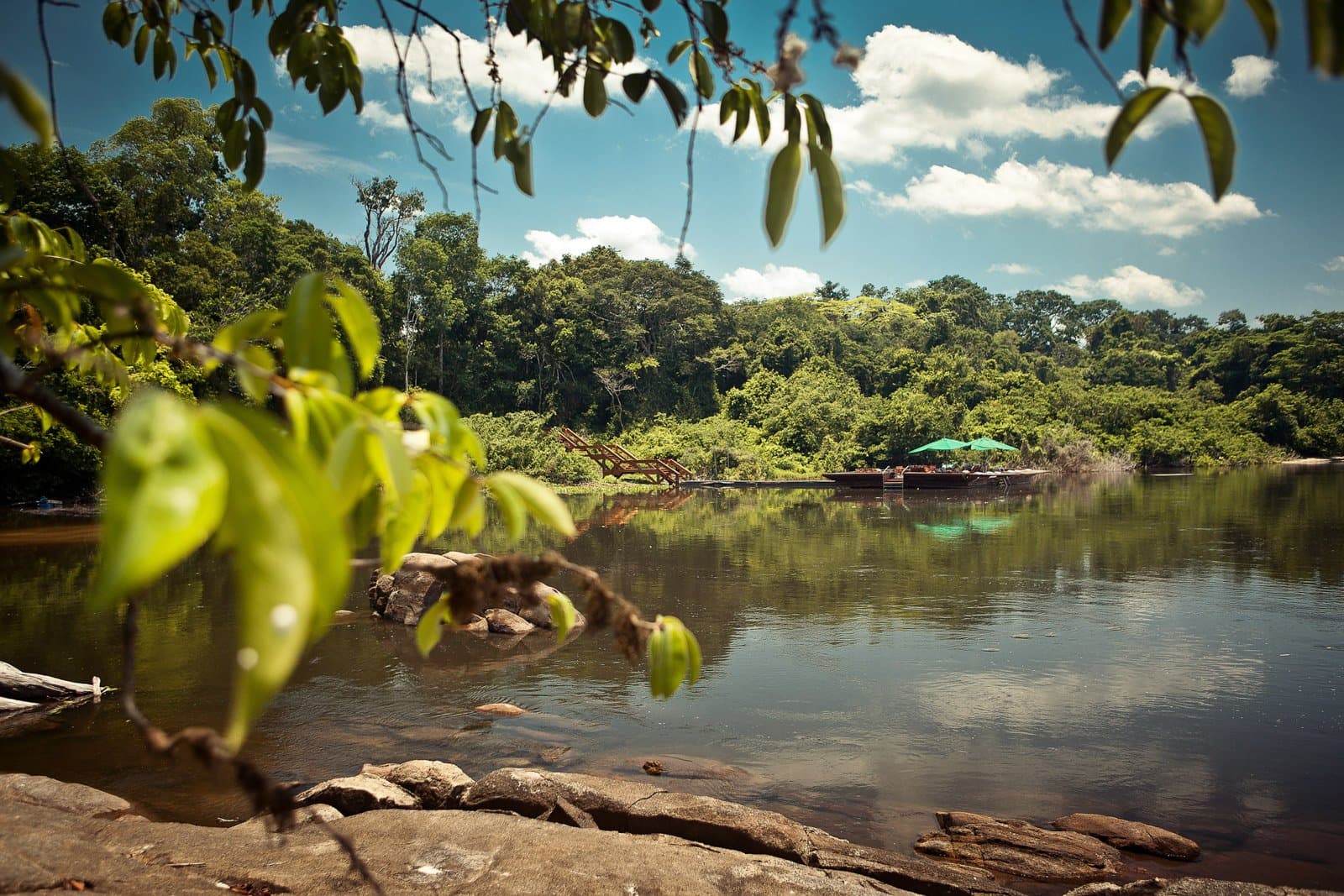 Ein Flussufer, an dem die Zeit einfach aufhört zu zählen. Ein ruhiger Fluss spiegelt den dichten Regenwald wider, während das schwimmende Dock des Cristalino Jungle Lodge mit grünen Sonnenschirmen durch das Laub im Vordergrund sichtbar wird