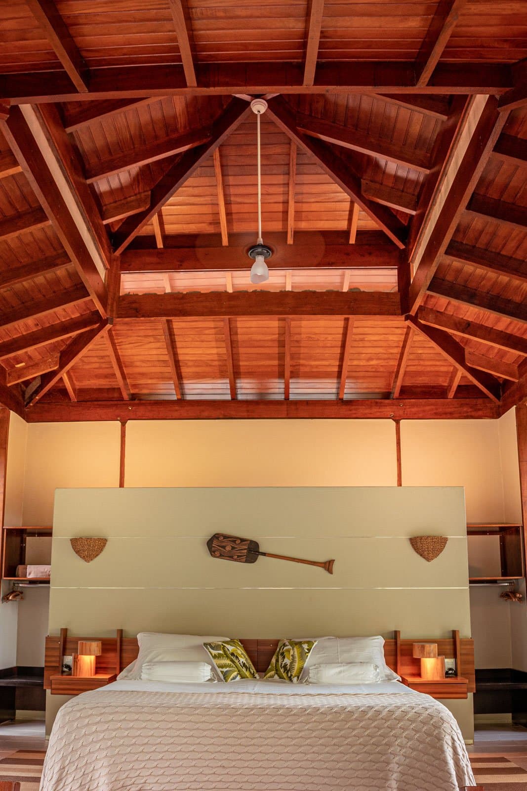 Warmes Holz, hohe Dachbalken und ein Paddel an der Wand, das Zimmer trägt den Regenwald in sich. Ein hohes, gewölbtes Holzdach überspannt ein Doppelbett im Cristalino Jungle Lodge, flankiert von leuchtenden Holznachttischen und einem dekorativen Paddel an der Kopfteilwand