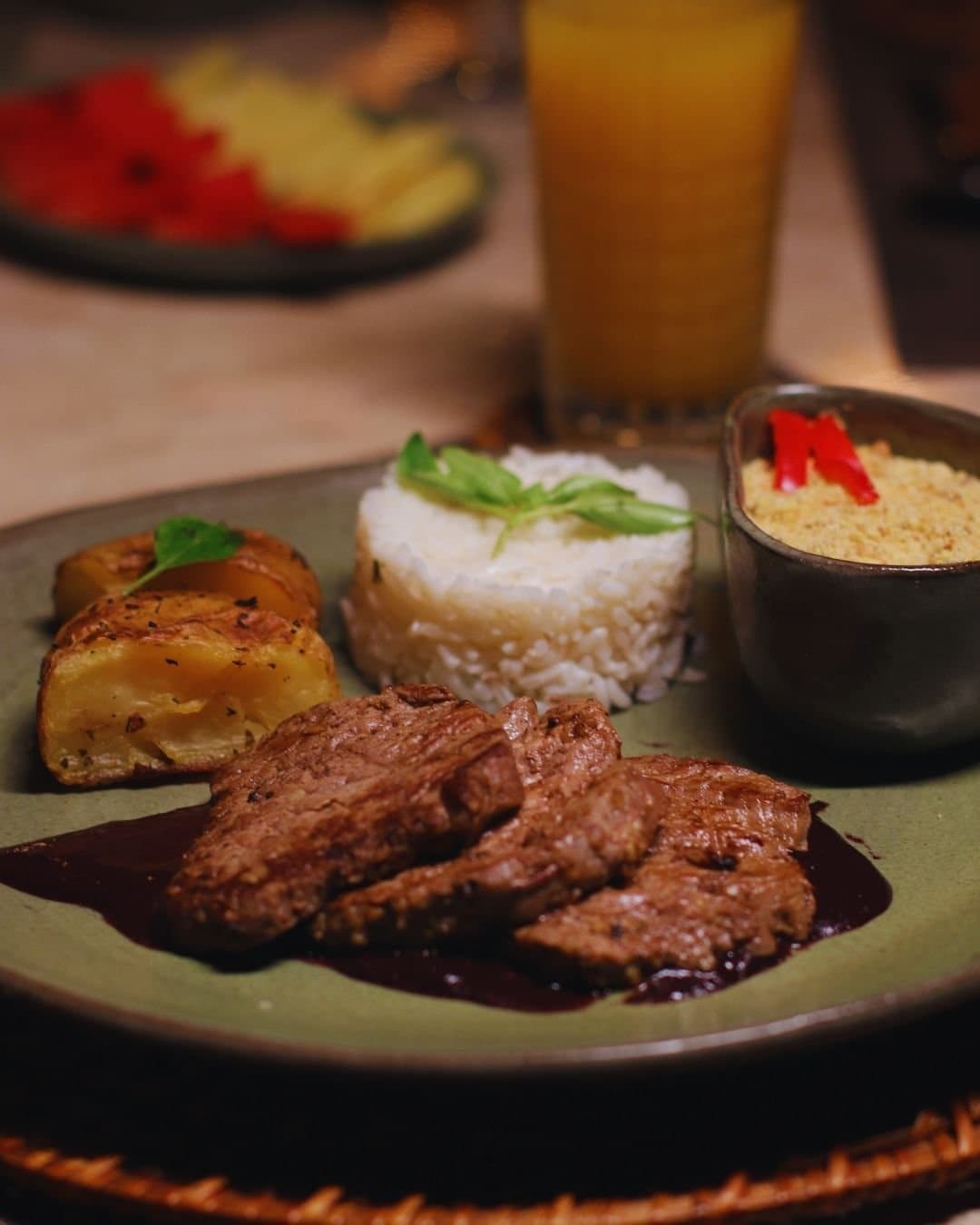Brasilianische Hausmannskost, die wirklich satt und glücklich macht. Abendessen in der Juma Amazon Jungle Lodge: gegrillte Rindfleischstreifen in dunkler Sauce, geformter Reis mit frischen Kräutern, gebratene Kartoffelspalten und eine Schüssel Farofa mit roten Paprikastreifen, dazu ein Glas Orangensaft