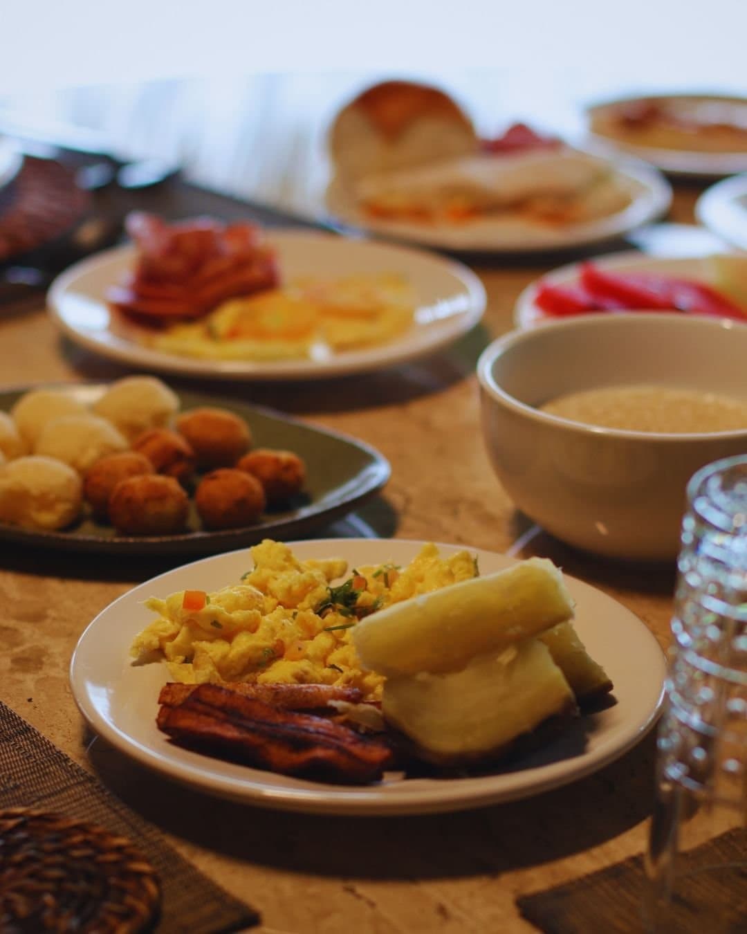 Ein ordentliches Frühstück, bevor der Dschungel das Programm übernimmt. Ein reichhaltiges Frühstücksbuffet in der Juma Amazon Jungle Lodge mit Rühreiern, knusprigem Speck, gekochtem Maniok, gepökeltem Fleisch, frischer roter Paprika, gebratenem Gebäck, Brötchen und einem Schälchen Brei auf einem Holztisch