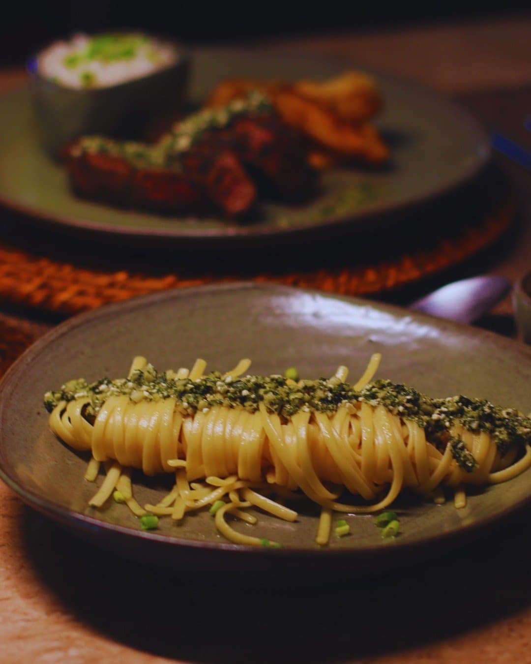 Wenn der Dschungel draußen rauscht, schmeckt Pasta gleich nochmal besser. Ein Nest aus Linguine-Pasta mit Kräuter- und Saatenkruste auf einem rustikalen Keramikteller in der Juma Amazon Jungle Lodge, im Hintergrund verschwommen ein Teller mit gegrilltem Fleisch