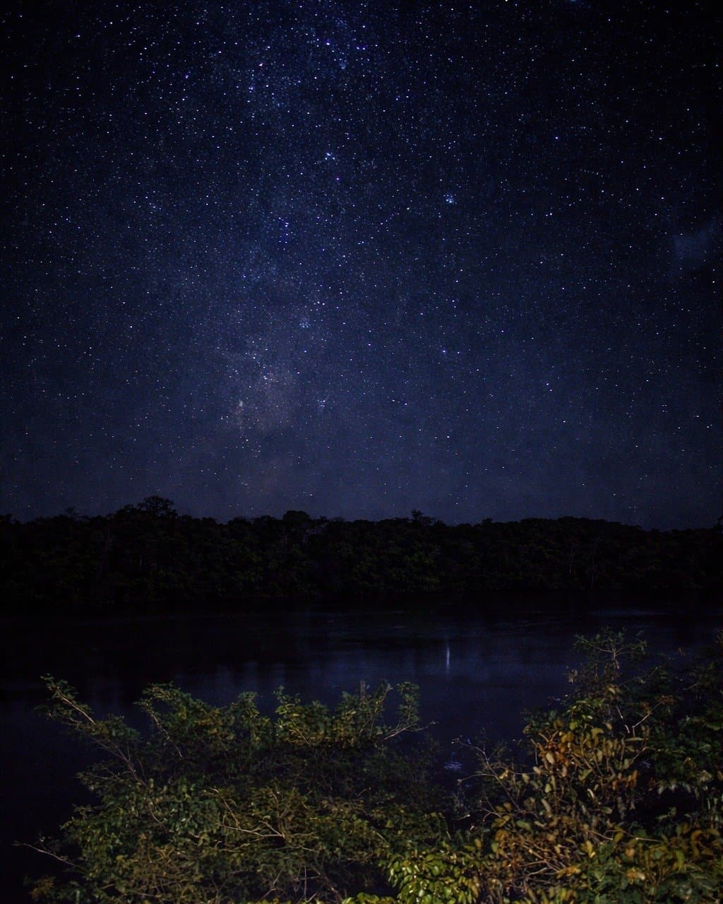 So sieht der Himmel aus, wenn niemand ihn anschaltet. Die Milchstraße spannt sich über einen sternklaren Himmel über einem dunklen Dschungelfluss im Juma Amazon Jungle Lodge, der Galaxienkern spiegelt sich schwach im stillen Wasser