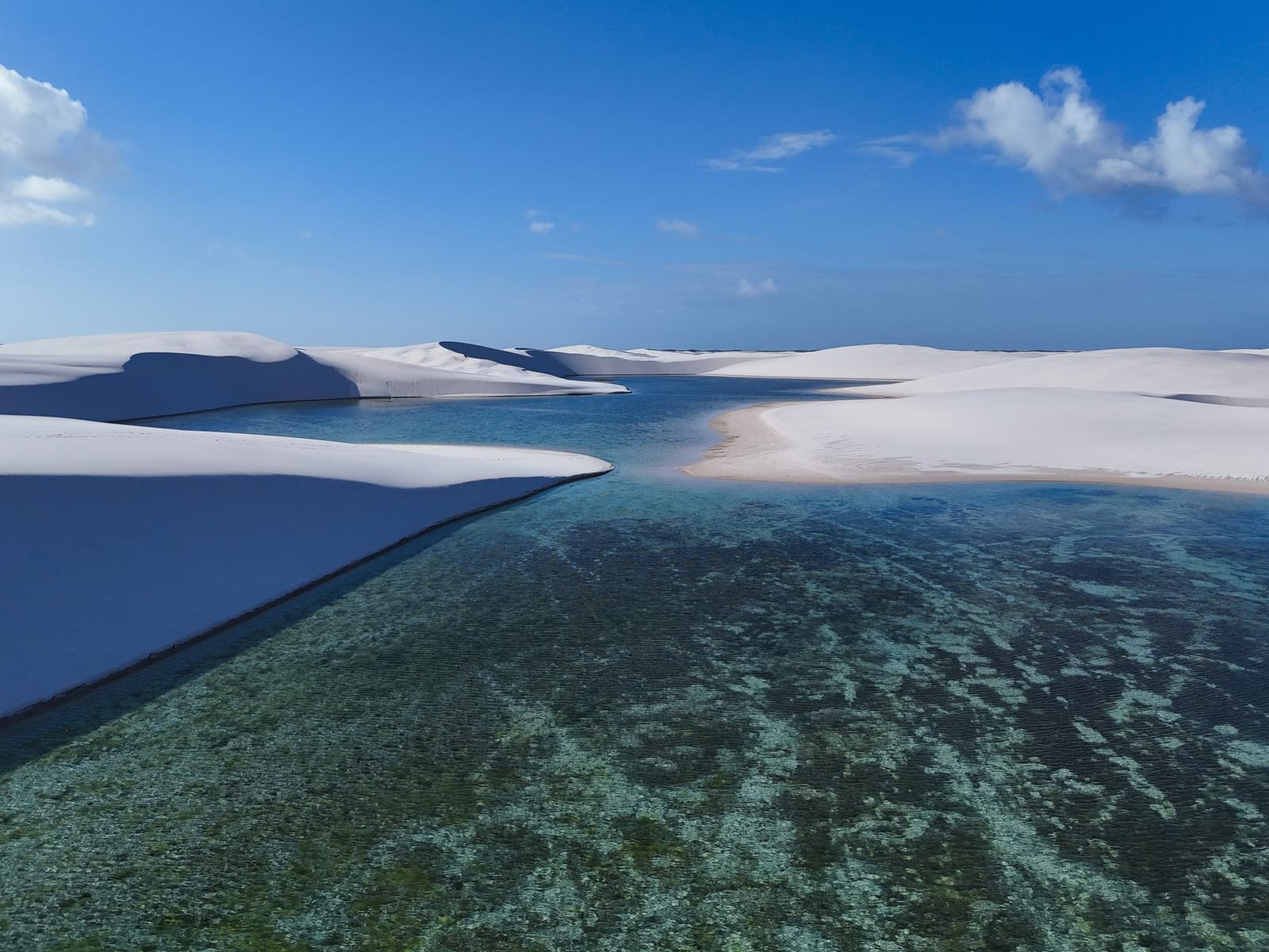 Wit zand en helder water, elk met hun eigen kant van het verhaal. Luchtfoto van een kristalheldere turquoise lagune genesteld tussen uitgestrekte witte zandduinen onder een diepblauwe lucht tijdens een Lençóis Maranhenses trip