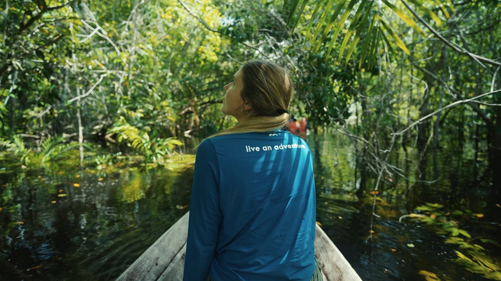 Kein Lärm, kein Signal, nur das leise Gleiten durch den Amazonas-Urwald. Eine Reisende sitzt im Bug eines Holzkanus und blickt in den dichten Blätterwald des überfluteten Amazonas-Urwalds während einer Bootsfahrt ab einer Luxuslodge