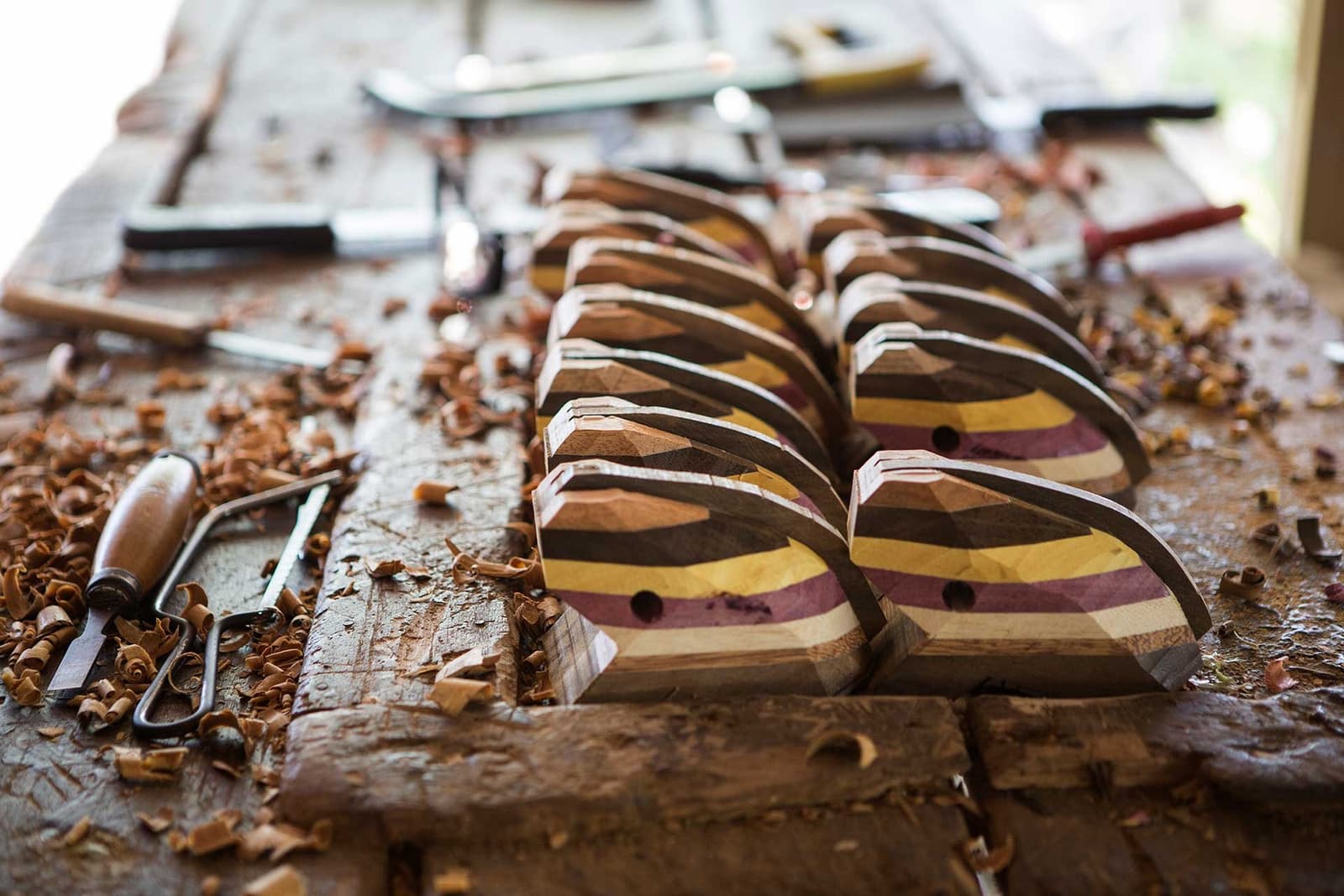 Handwerk, das riecht und klingt und bleibt. Mehrere handgefertigte Holzobjekte aus farbig laminierten Holzschichten liegen auf einer Werkbank, umgeben von Holzspänen und Schnitzwerkzeugen – ein Zeugnis lokalen Kunsthandwerks nahe einer Luxuslodge im brasilianischen Amazonas