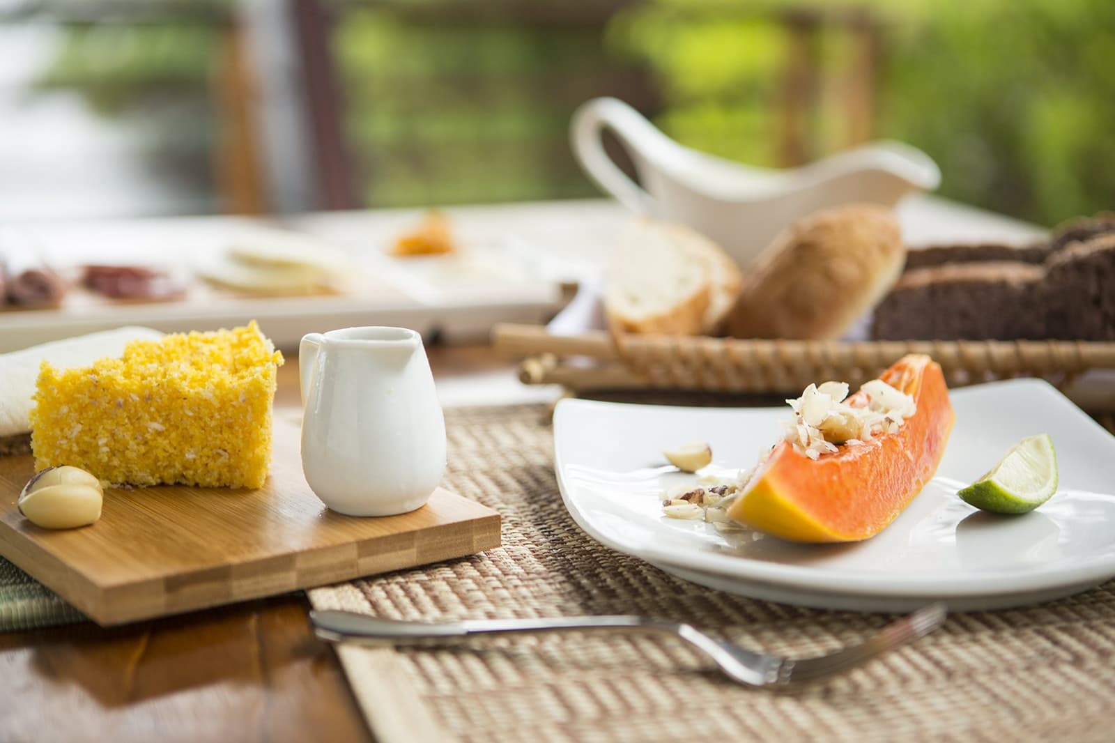 Das Frühstück allein wäre schon eine Reise wert. Frische Papaya mit Nüssen und Limette sowie ein Stück gelber Maiskuchen auf einem Holzbrett, serviert beim Frühstück in einer Luxuslodge im brasilianischen Amazonasgebiet, mit üppigem Grün im Hintergrund