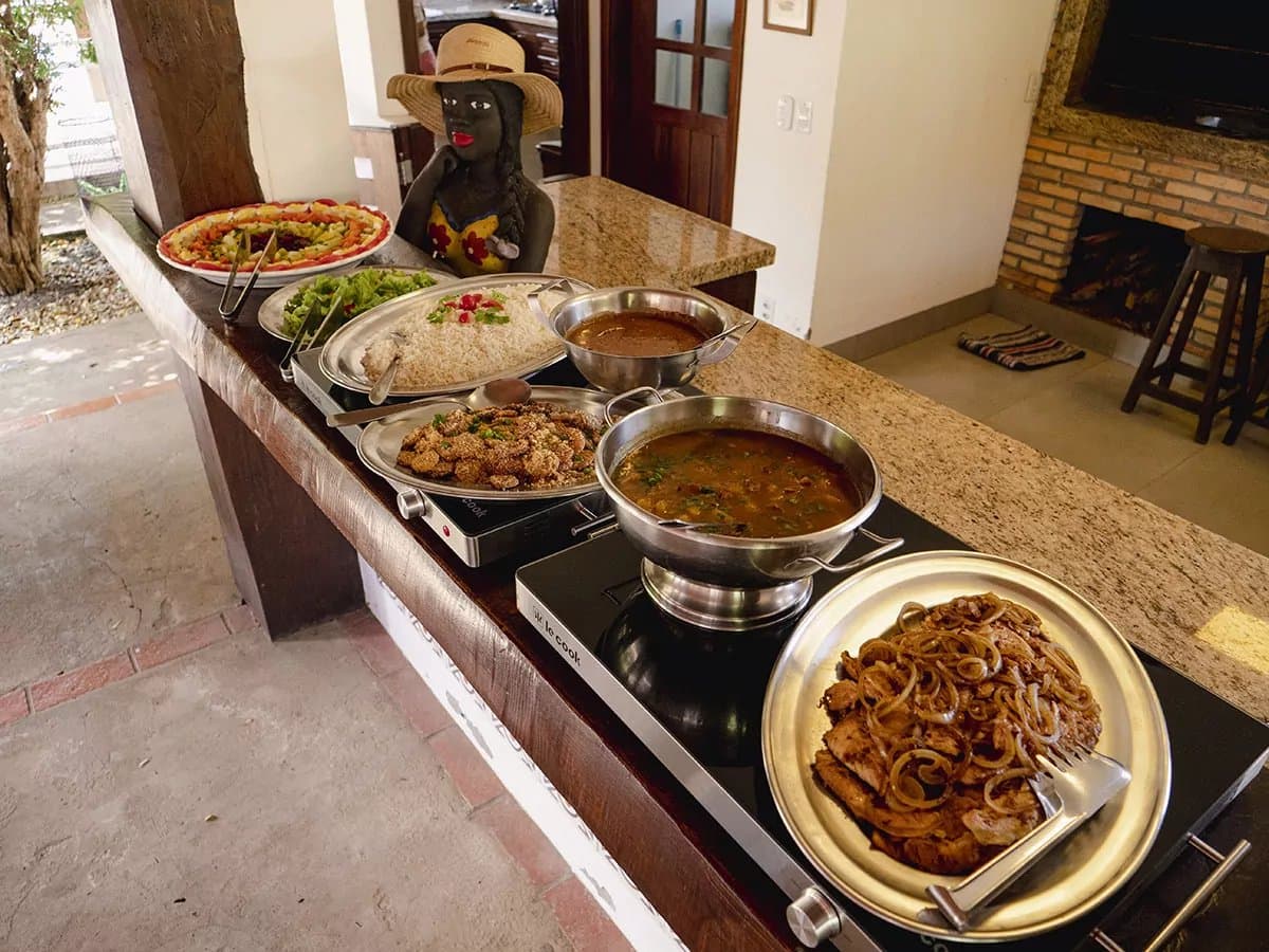 Lunch at the lodge hits different after a morning in the field. A granite-topped buffet counter laid with steaming pans of stew, seasoned meat with caramelised onions, rice, fried bites, salads and a colourful fresh-fruit platter — hearty Brazilian lodge cooking on a Pantanal Bonito tour