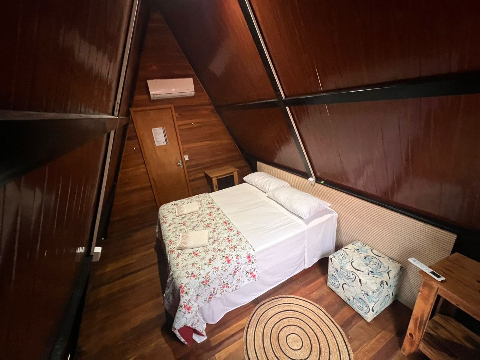 Rustikal, ordentlich, und nach einem langen Safariage genau das Richtige. Innenraum einer A-Rahmen-Holzhütte mit Doppelbett, geblümter Tagesdecke, Holzboden und Klimaanlage auf einer Pantanal-Jaguar-Budget-Safari