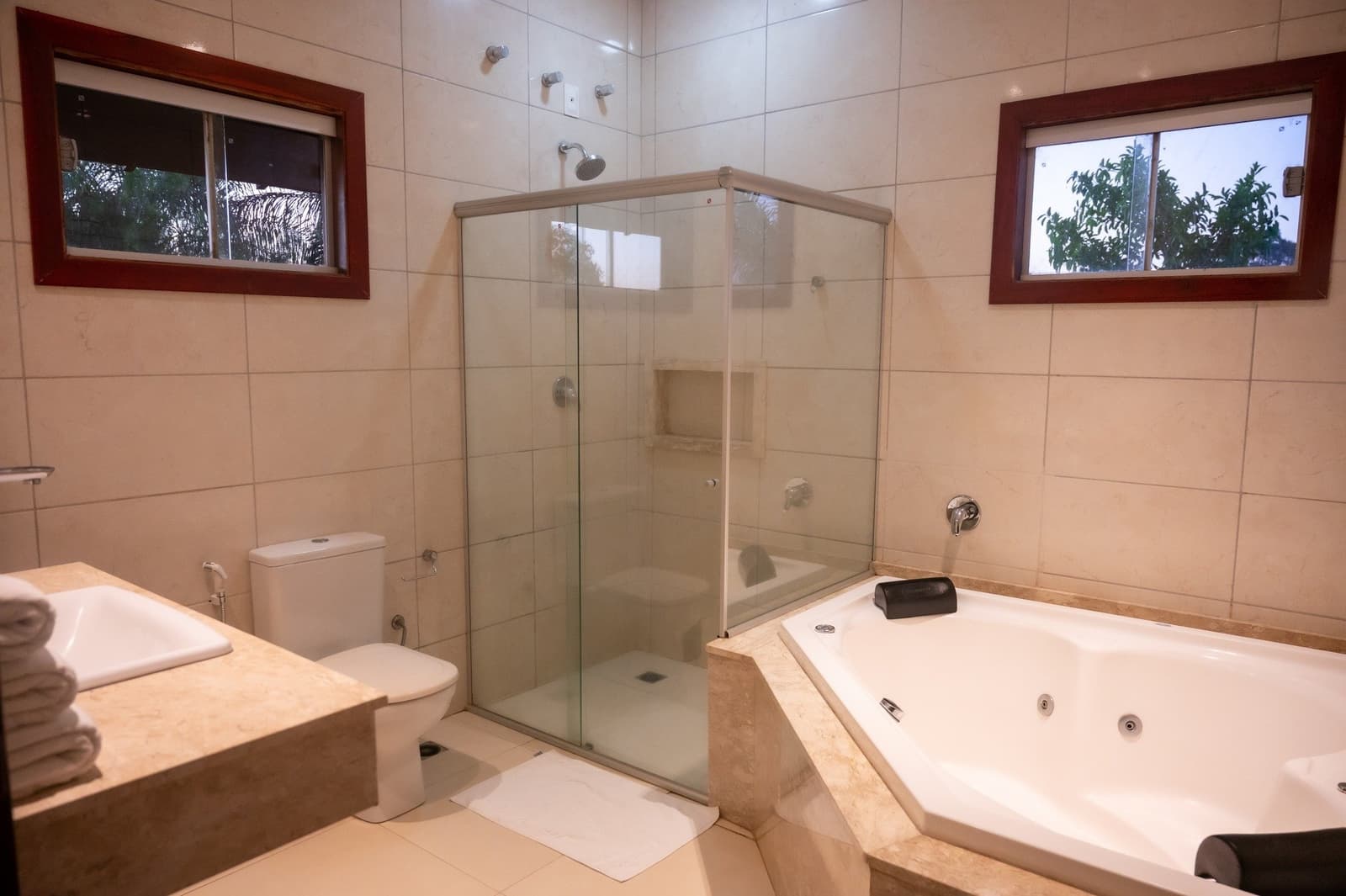 Nach einem Tag im Sumpf fühlt sich eine Badewanne wie eine Belohnung an. Geräumiges Badezimmer einer Lodge beim Pantanal-Jaguar-Budget-Safari mit Glasdusche, Eckwhirlpool, Marmorwaschtisch und Fenstern mit Blick ins Grüne