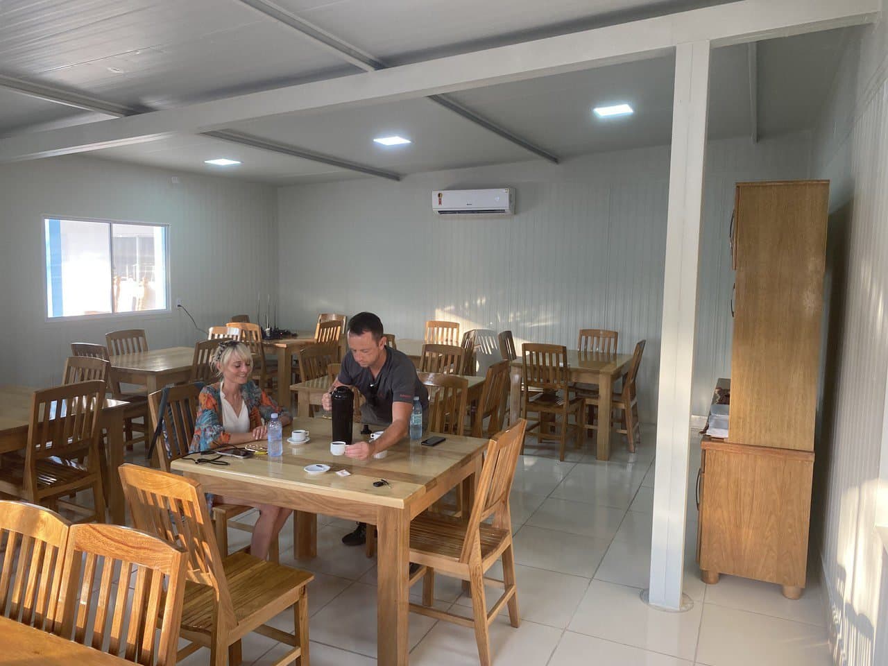 Kaffee, ein ruhiger Tisch und viel zu erzählen vom Morgen im Pantanal. Zwei Reisende trinken Kaffee an einem Holztisch in einem sauberen, klimatisierten Speisesaal während einer Pantanal-Jaguar-Budget-Safari