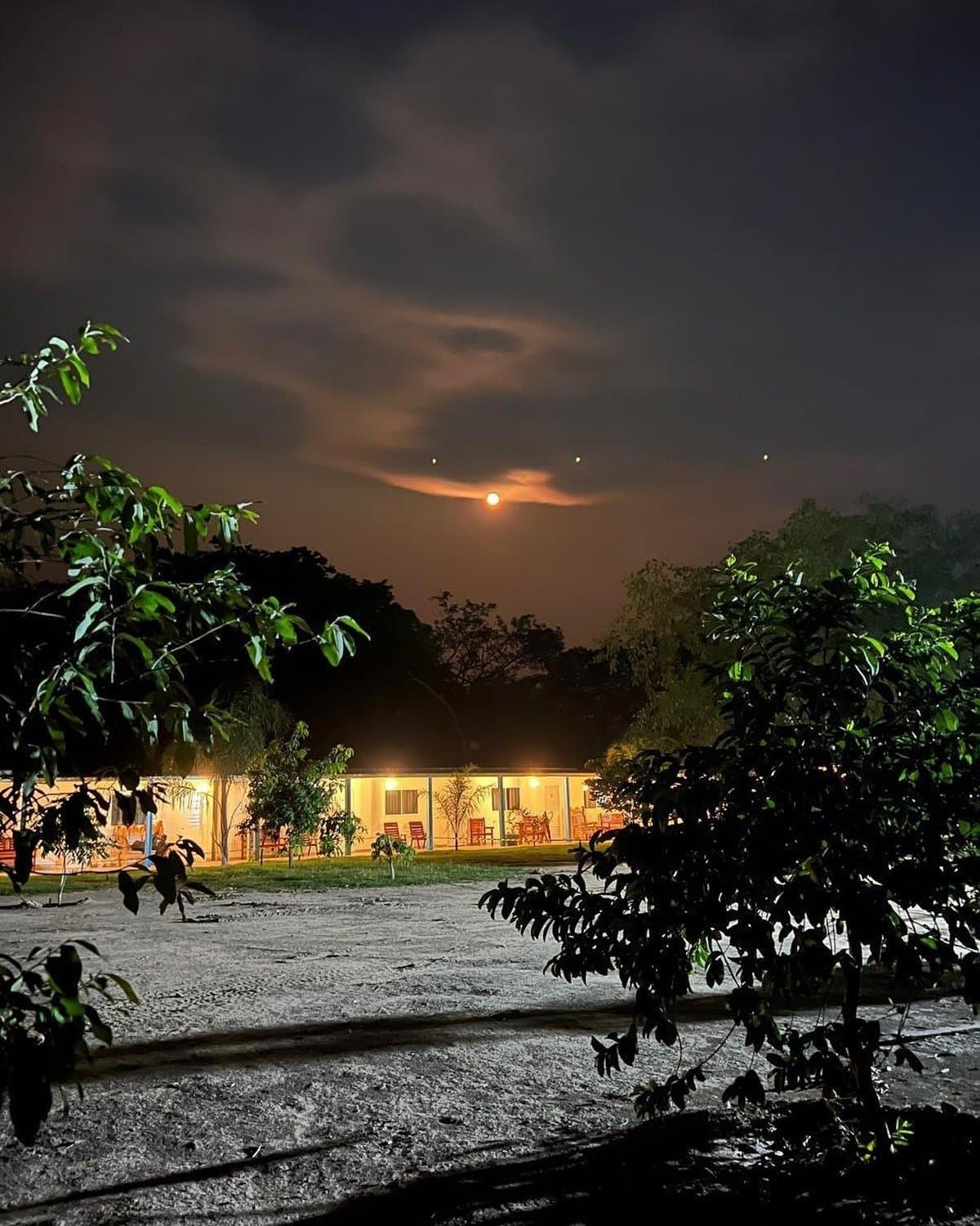 Die Lodge leuchtet sanft, der Rest gehört der Nacht. Eine warm beleuchtete Lodge leuchtet unter einem dramatischen Nachthimmel mit aufgehendem Vollmond über tropischen Bäumen