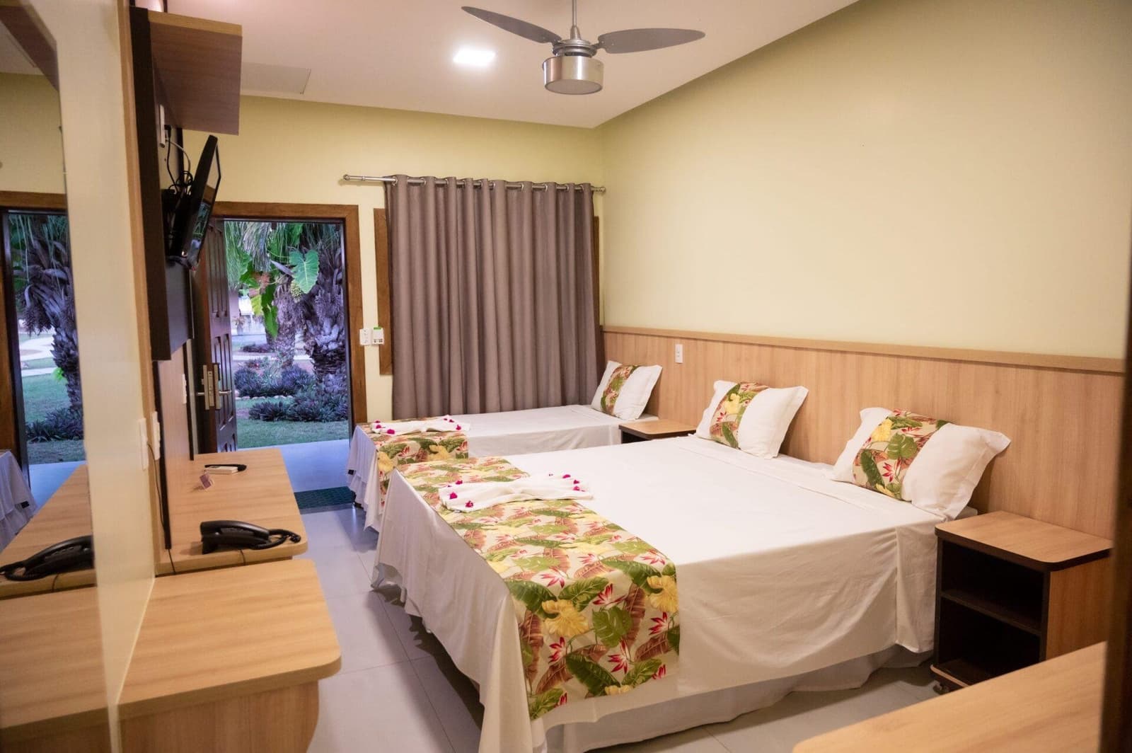 Alles, was man nach einem langen Tag draußen wirklich braucht. Dreibettzimmer auf einer Pantanal-Jaguar-Budget-Safari mit zwei Doppelbetten, tropischen Bettwäsche-Läufern, Deckenventilator und geöffneter Tür zum üppigen Garten