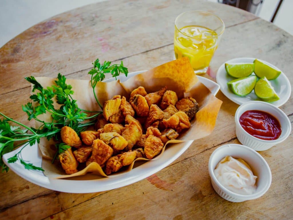 Knusprig, heiß und unwiderstehlich, die perfekte Stärkung zwischen den Ausfahrten. Ein Teller goldener frittierter Häppchen mit frischer Petersilie, Limettenspalten, Ketchup und Cremesoße auf einem rustikalen Holztisch