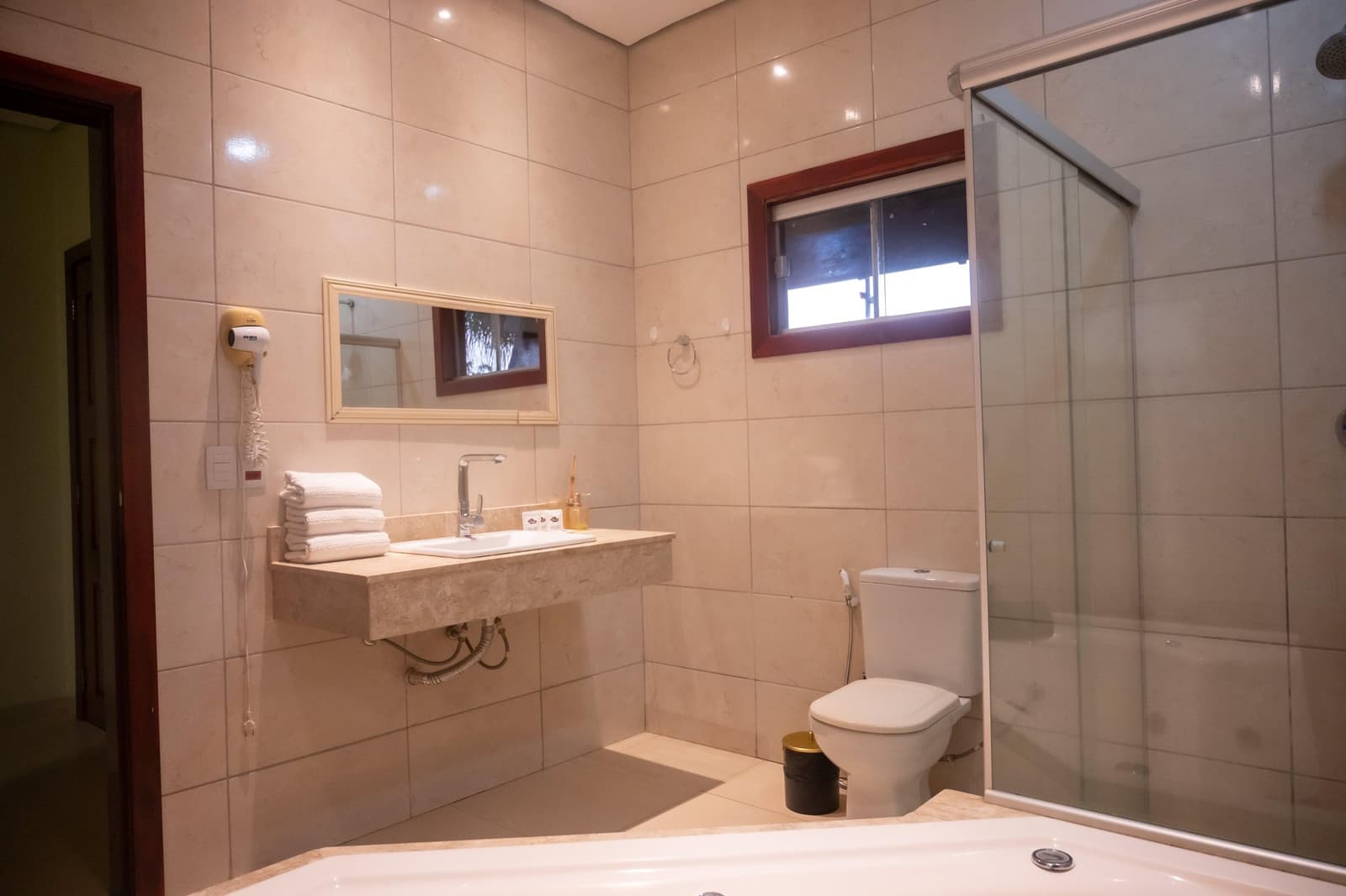 Verse handdoeken en een warme douche, precies wat je nodig hebt na een dag in het veld. Ruime privébadkamer van een lodge op de Pantanal-tour vanuit Cuiabá, met marmeren wastafelblad, gevouwen witte handdoeken, glazen douche, bad en wandföhn