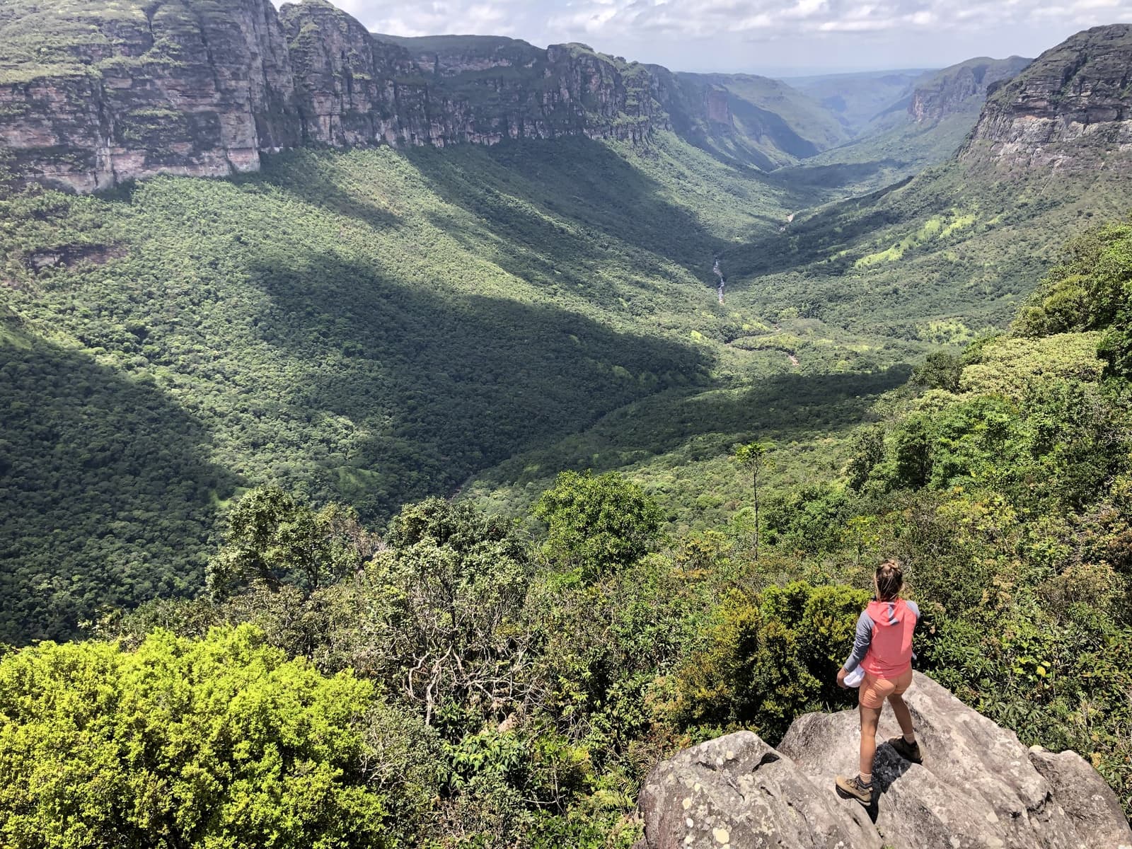 O Vale do Pati não pressa ninguém, e você vai entender por quê. Uma caminhante de pé sobre uma rocha contempla o vasto canyon florido da trilha do Vale do Pati, com paredões de arenito e uma cachoeira ao fundo do vale