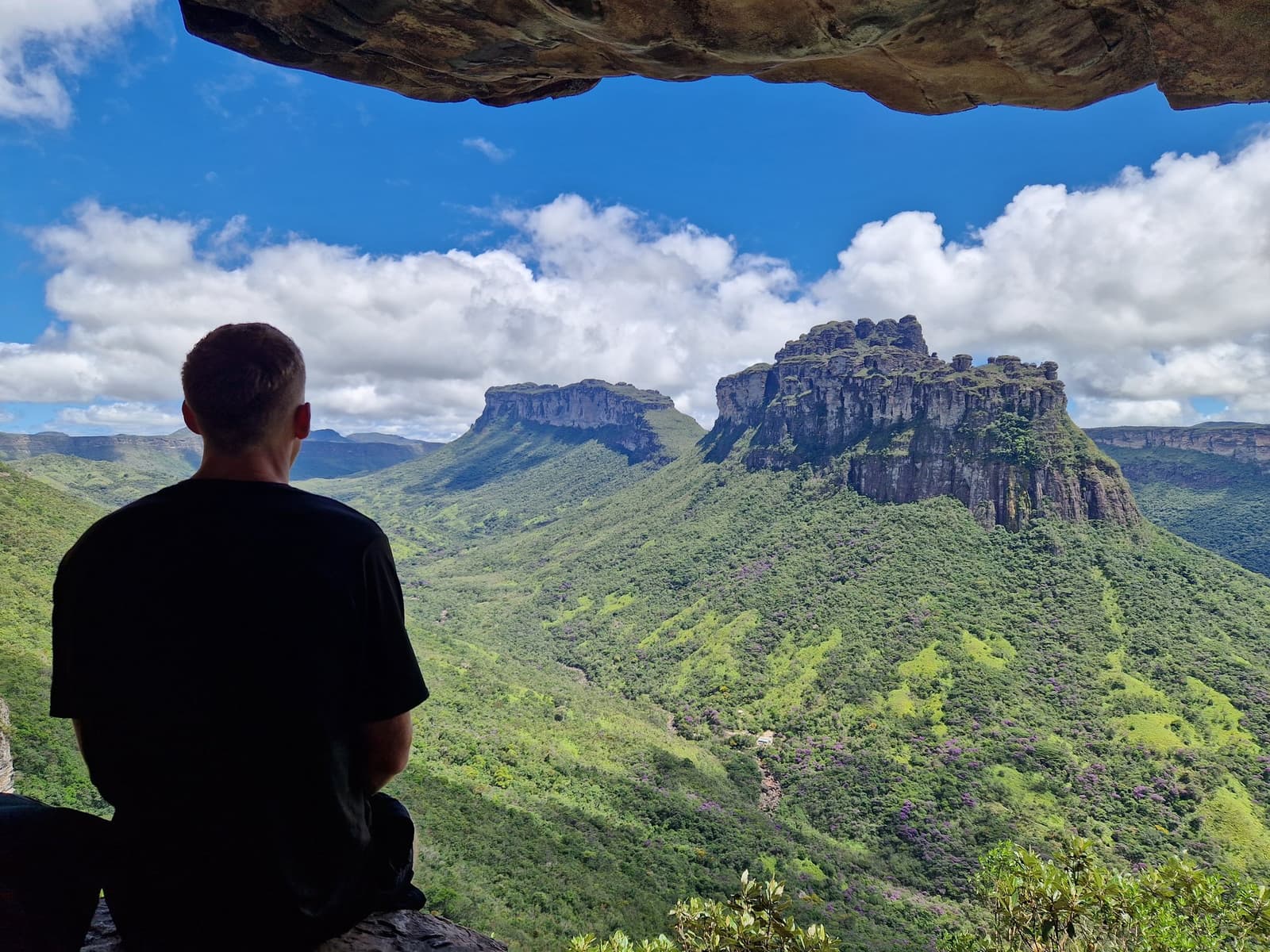 O Vale do Pati não entrega essa vista de graça. Um caminhante sentado sob uma laje rochosa contempla a imponente mesa de arenito do Morro do Castelo erguendo-se sobre colinas verdes durante a trilha do Vale do Pati na Chapada Diamantina