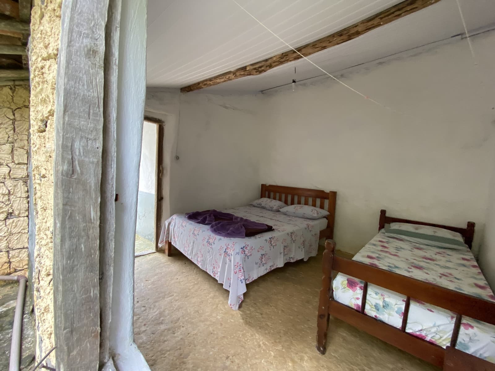 Simples assim. Depois de um dia inteiro de trilha, a cama já basta. Quarto compartilhado simples com duas camas de madeira e roupa de cama floral em uma pousada familiar rústica de pedra na trilha do Vale do Pati