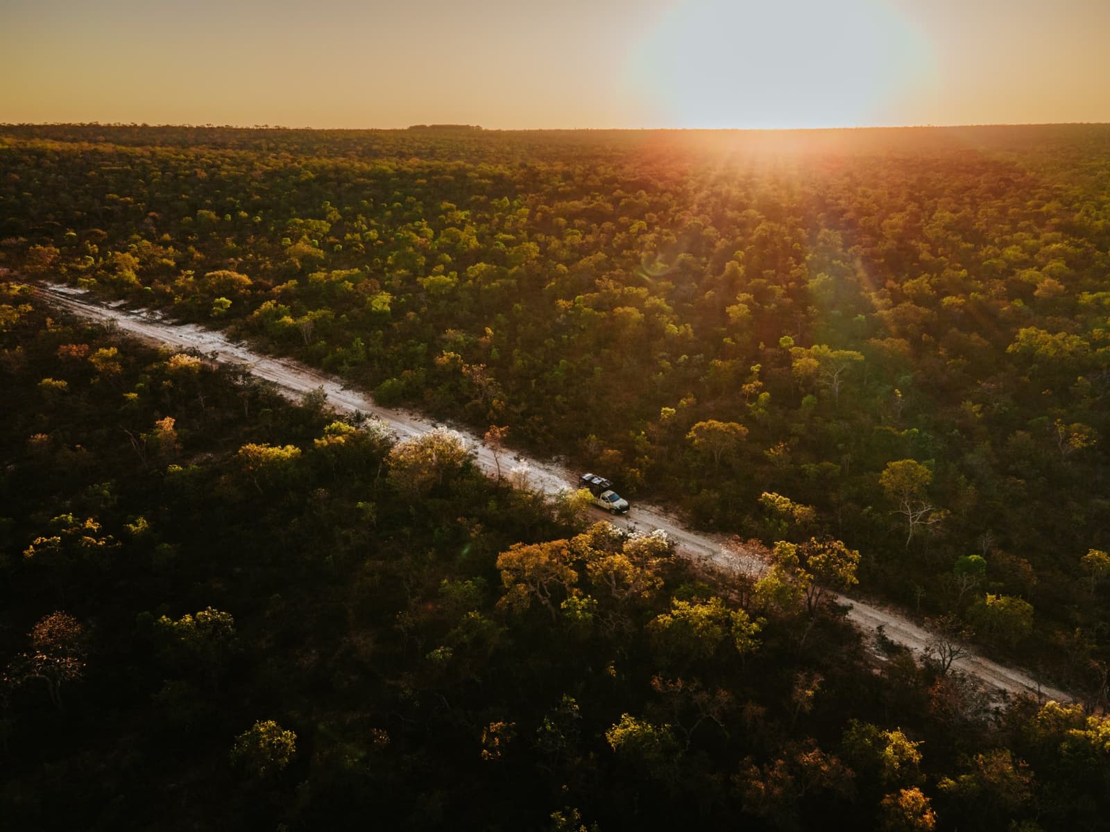 Une piste, des arbres à perte de vue, et cette lumière de fin de journée qu'on n'oublie pas de sitôt. Vue aérienne de deux véhicules 4x4 sur une piste de sable traversant la forêt dense du Cerrado à la Pousada Trijunção, baignée d'une lumière dorée au coucher du soleil