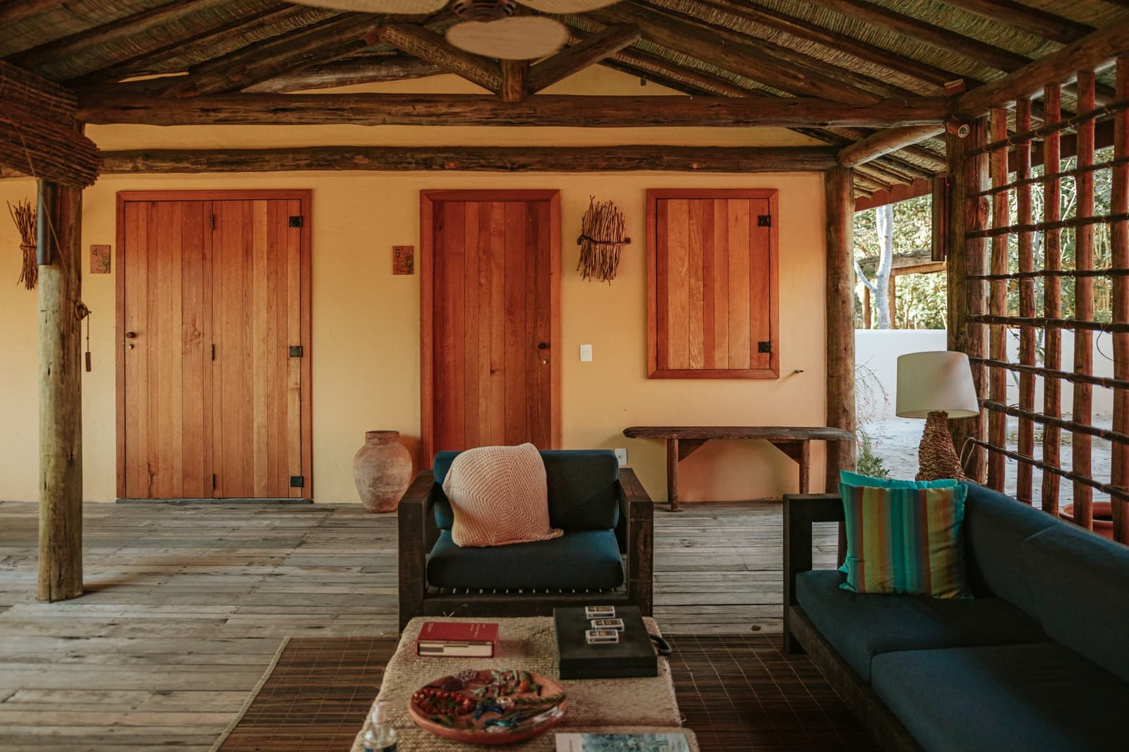 Le genre de salon où on pose les affaires et on ne repart pas tout de suite. Véranda couverte en plein air de la Pousada Trijunção avec fauteuils bleu sarcelle, piliers en bois brut et portes artisanales en bois chaud