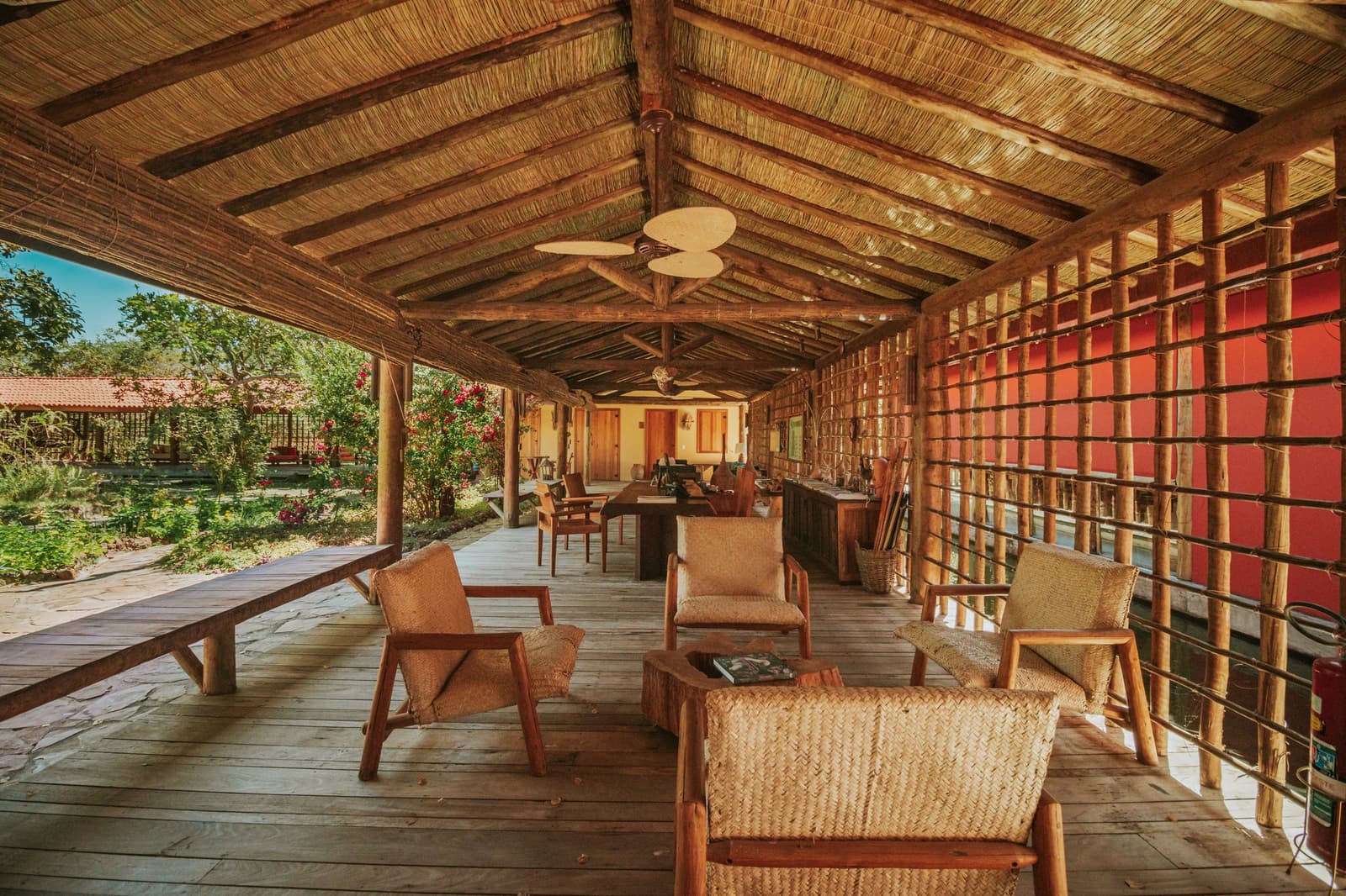 Le genre de terrasse où les récits de safari s'étirent aussi longtemps que les soirées. Terrasse couverte de la Pousada Trijunção avec fauteuils en rotin tressé, plancher en bois rustique, toit en chaume et vue sur un jardin luxuriant