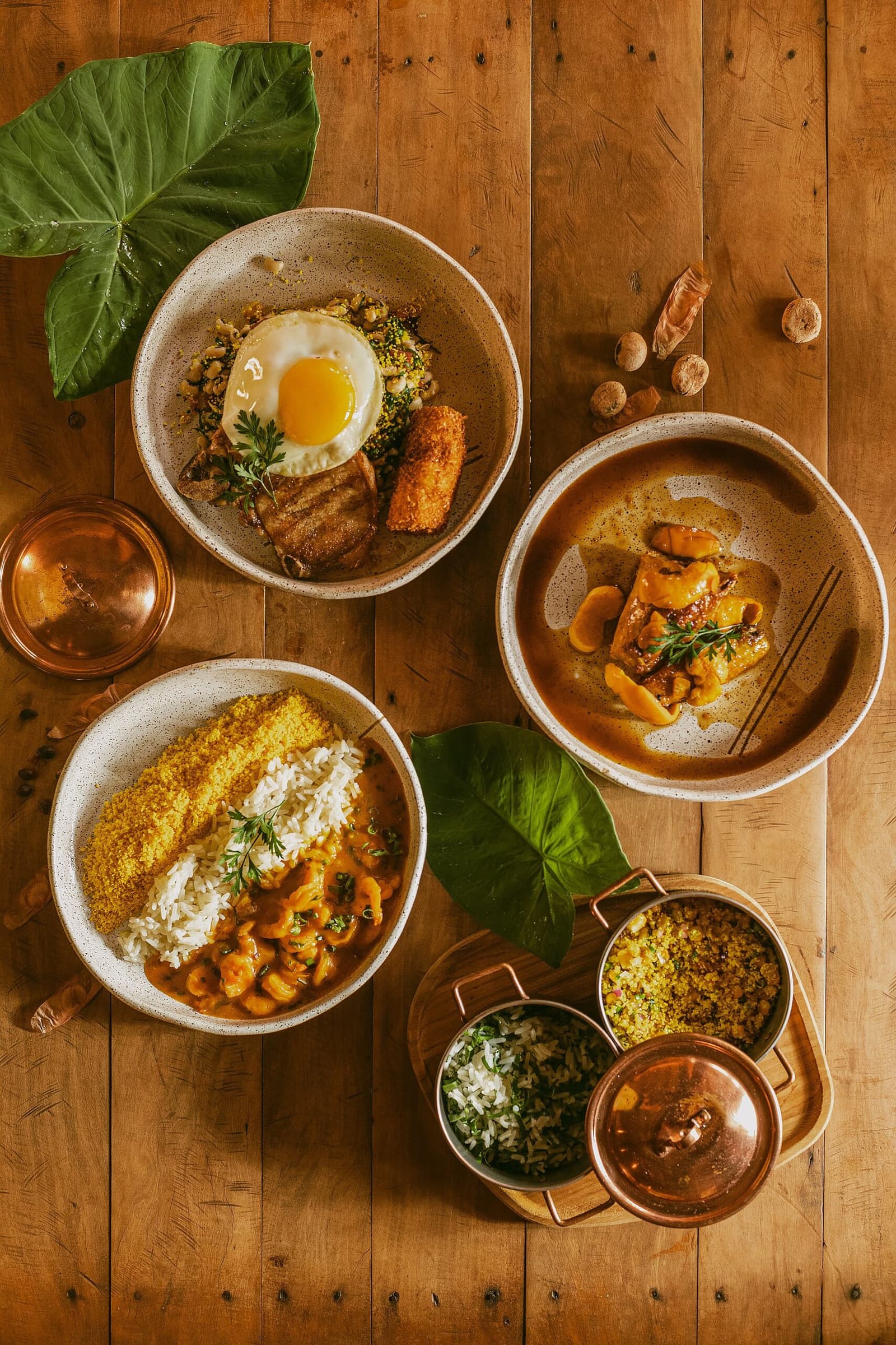 Un repas comme ça, et la sieste s'impose d'elle-même. Quatre bols en céramique de plats brésiliens traditionnels servis à la Pousada Trijunção : moqueca de crevettes avec riz et farofa, bol de riz au plat avec du porc croustillant, ragoût de viande et mini-cocottes en cuivre sur une table en bois