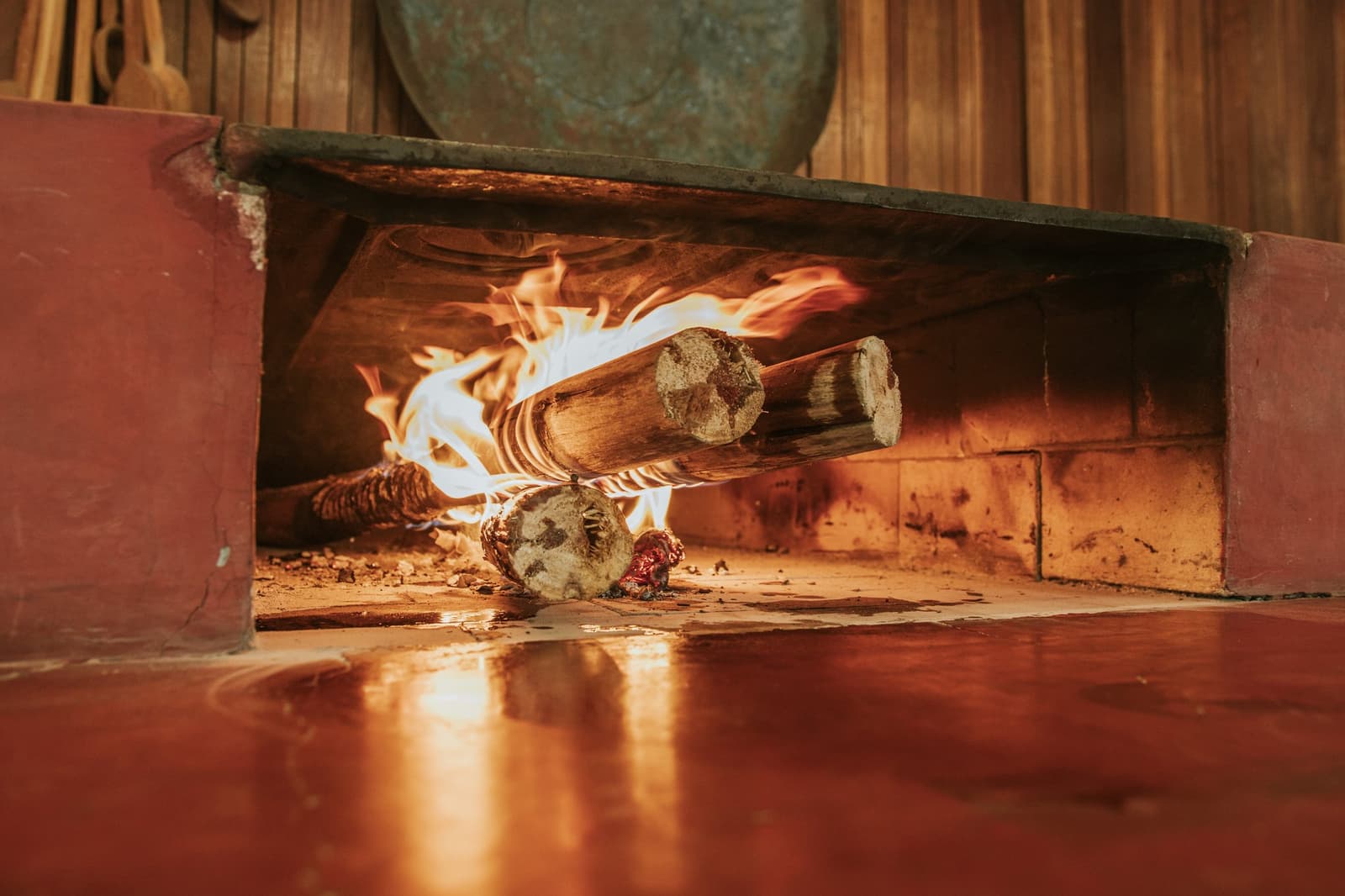 Tout commence par ce feu, bien avant que l'assiette arrive. De grosses bûches en feu dans un foyer traditionnel en pierre de la Pousada Trijunção, avec la lumière chaude des flammes se reflétant sur le sol rouge poli