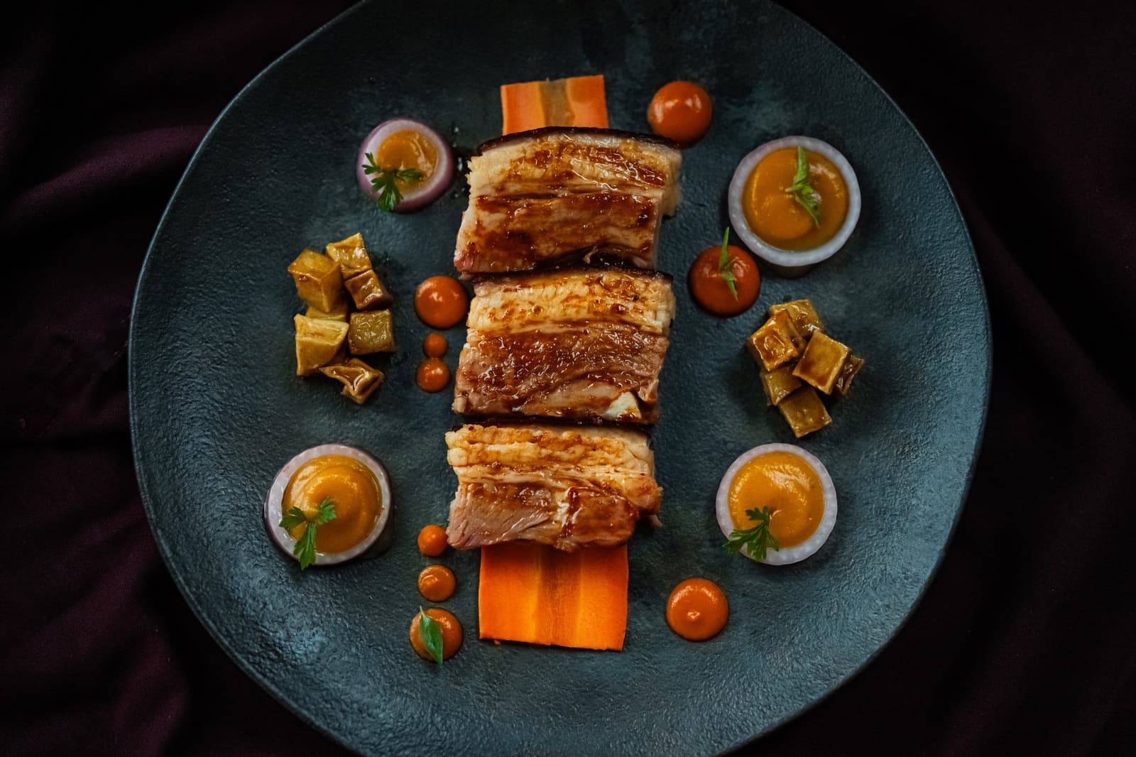 River life has its own rhythm, and dinner keeps pace. Three glazed slices of roasted meat rested on carrot ribbons, surrounded by golden sauce cups, cherry tomatoes and braised vegetable cubes on a teal plate — fine dining aboard the untamed amazon cruise