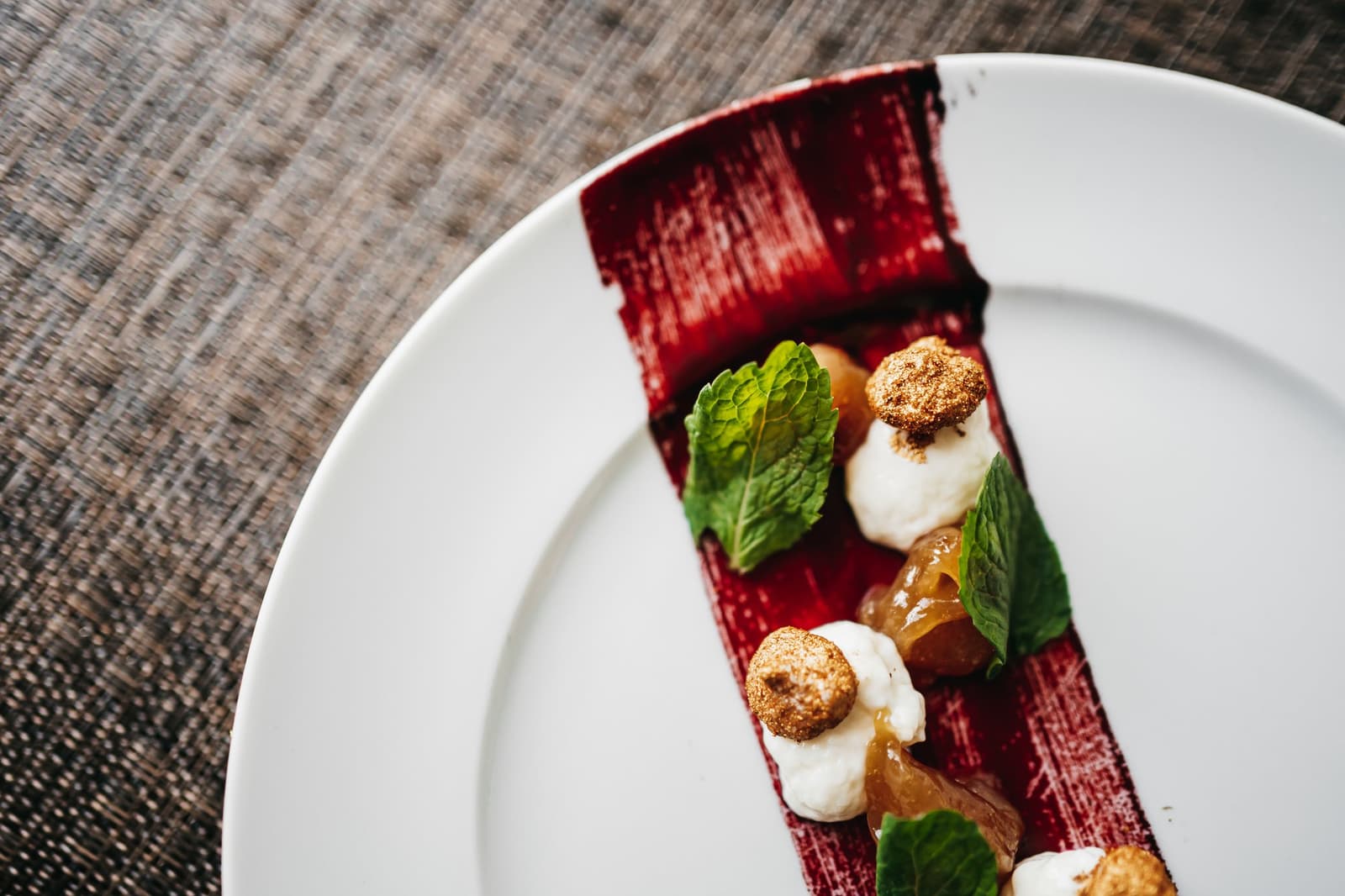 An Bord stellt sich heraus: Der Fluss liebt auch süße Überraschungen. Ein kunstvoll angerichtetes Dessert auf einem weißen Teller: ein tiefroter Riegel, belegt mit Sahnehäufchen, goldenen Krümelkugeln, durchscheinenden Fruchtstücken und frischen Minzblättern – serviert auf einer Luxus-Amazonas-Kreuzfahrt in Brasilien.