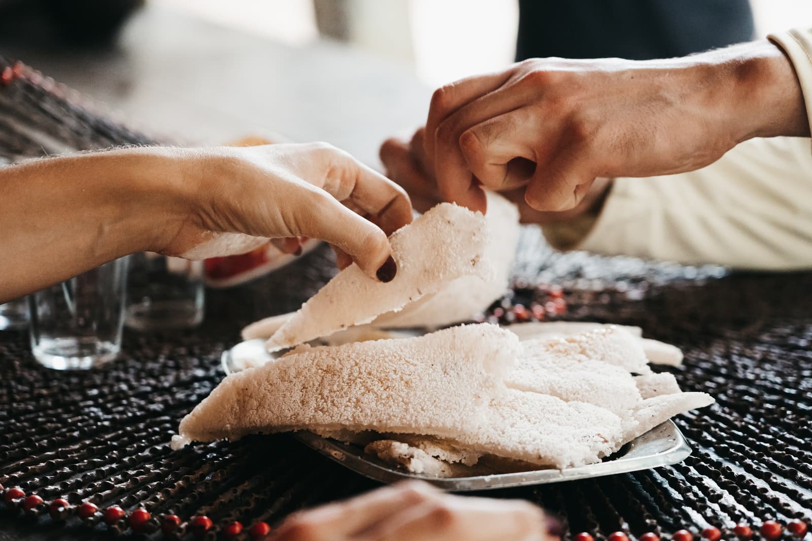 Mandiocabrot schmeckt am besten, wenn man es teilt. Kein Besteck nötig. Zwei Hände reißen gemeinsam dünnes Maniokfladenbrot über einem Teller auf einer geflochtenen Tischmatte auseinander – Teil des Vollpension-Erlebnisses auf einer Luxus-Amazonas-Kreuzfahrt in Brasilien.