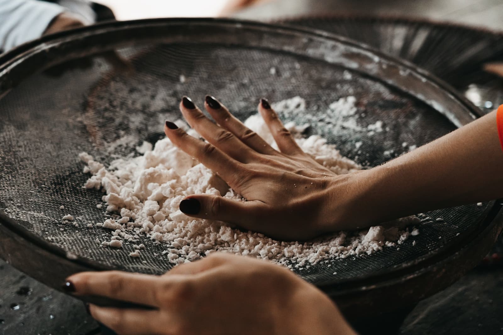 Maniokmehl, von Hand gesiebt. Hier zählt das Wissen, nicht das Rezept. Hände mit dunkel lackierten Nägeln drücken weißes Maniokmehl durch ein großes rundes Drahtsieb – eine traditionelle Technik, die bei Gemeinschaftsbesuchen auf einer Amazonas-Kreuzfahrt zu erleben ist