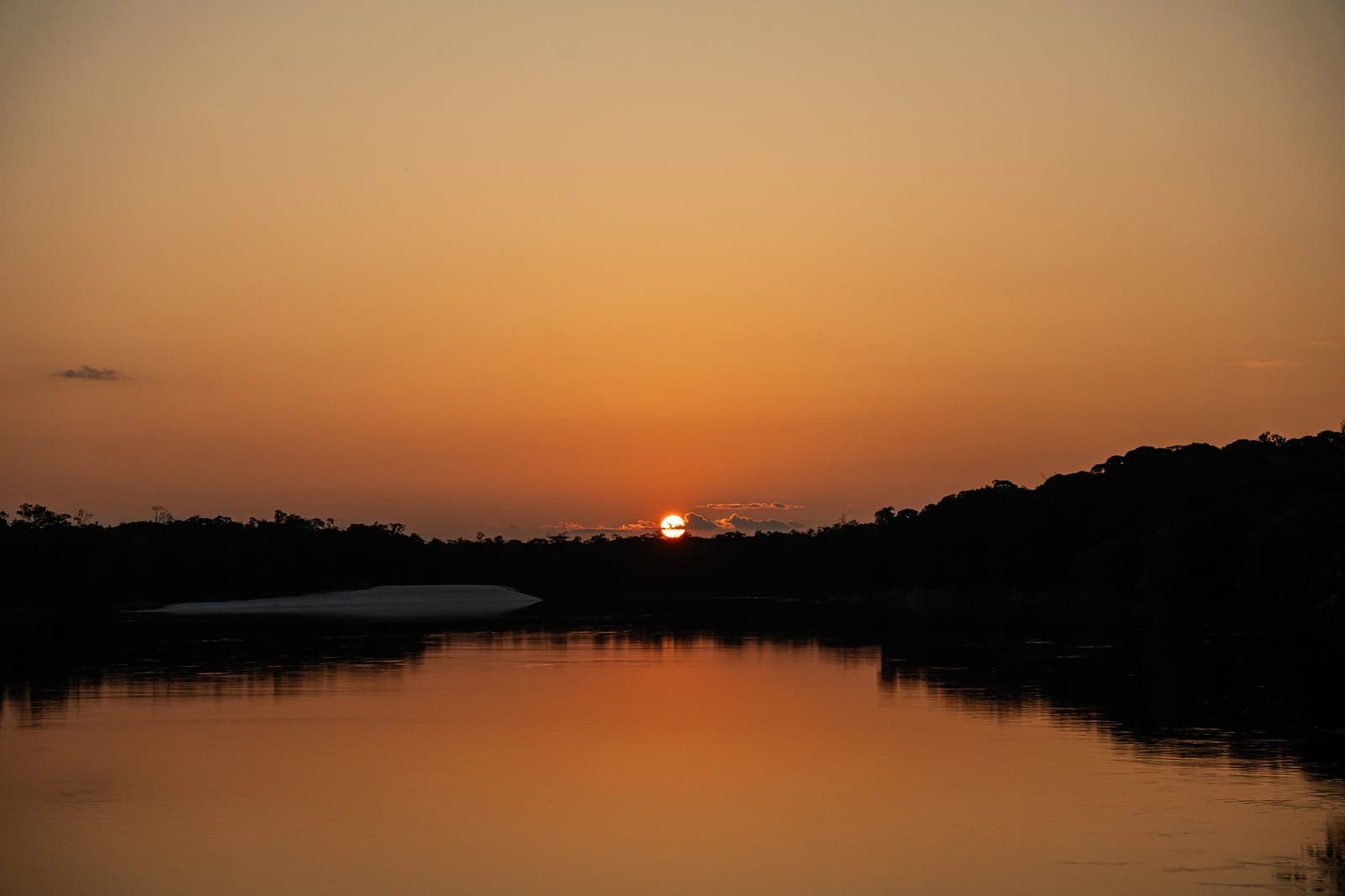 Manche Sonnenuntergänge brauchen einfach keine Worte. Tiefes Orangerot bei Sonnenuntergang über einem ruhigen Amazonas-Fluss, die Sonne berührt die silhouettierten Baumwipfel und spiegelt sich im stillen Wasser, eine weiße Sandbank am linken Ufer