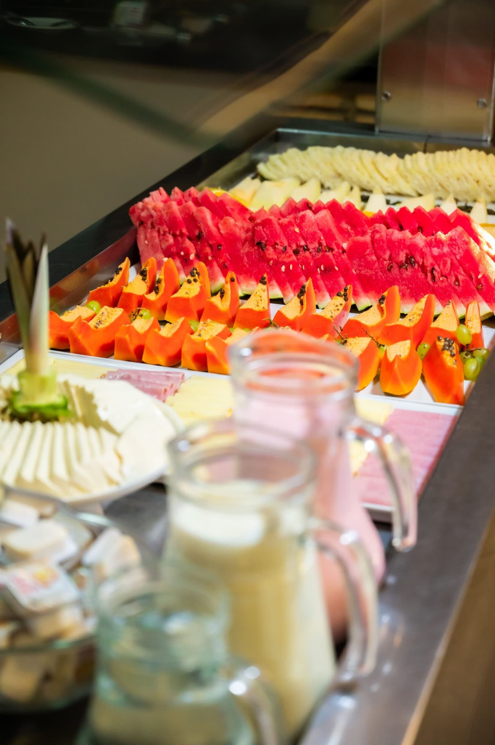 Papaya, watermelon, cheese, juice, the buffet does not mess around before a big day out. A hotel breakfast buffet on an amazon and pantanal tour, with rows of sliced watermelon and papaya arranged on a stainless-steel counter alongside sliced cheese, grapes, and glass pitchers of juice