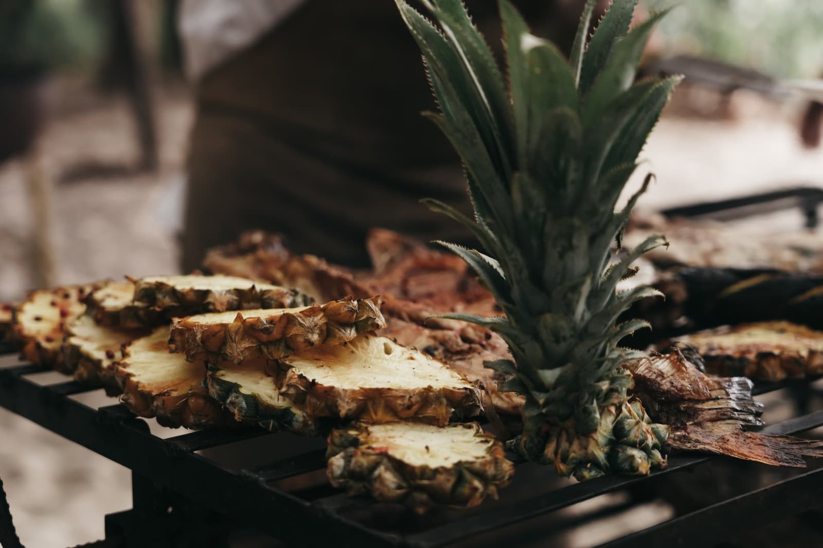 Ananas vom Grill, weil Dessert auf dem Fluss eigene Regeln hat. Frisch aufgeschnittene Ananashälften und eine ganze Ananaskrone auf einem Grillrost im Freien, karamellisiert über offenem Feuer als Teil der Vollpension an Bord einer Luxus-Amazonas-Kreuzfahrt in Brasilien