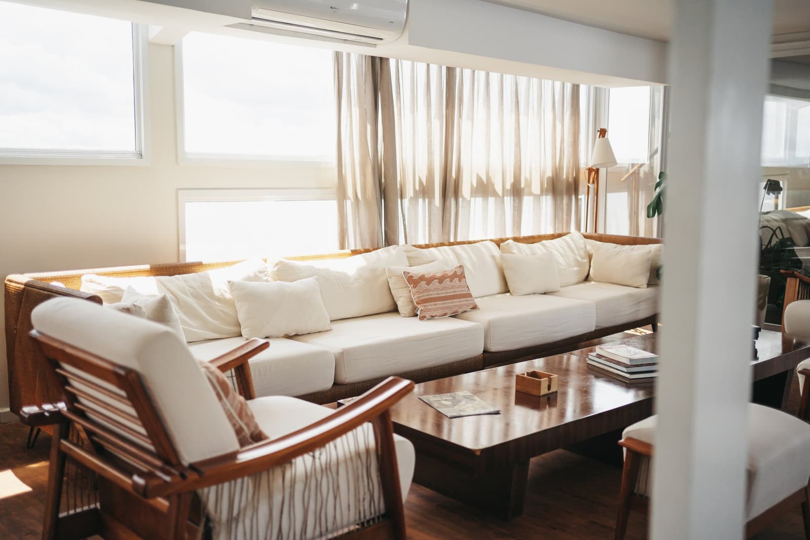 Ein Sofa, gutes Licht und kein Programm, manchmal ist das genug. Heller Salon auf einer Luxus-Amazonas-Kreuzfahrt in Brasilien mit einem breiten cremefarbenen Sofa, Holzsesseln, einem niedrigen Couchtisch mit aufgestapelten Büchern und leichten Leinenvorhängen