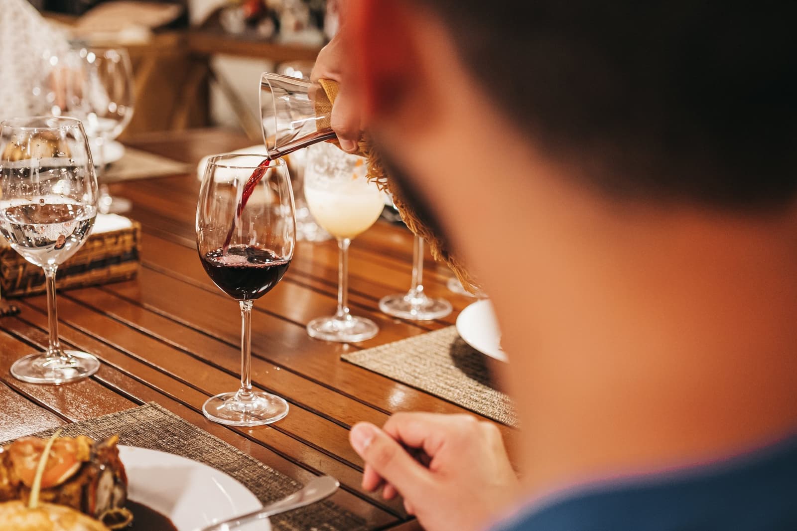 Wein eingeschenkt, Tisch gedeckt, der Fluss macht draußen sein Ding. Rotwein wird bei einem festlich gedeckten Abendessenstisch auf einer Luxus-Amazonas-Kreuzfahrt in Brasilien eingeschenkt, mit Wassergläsern, einem Cocktail und angerichtetem Essen