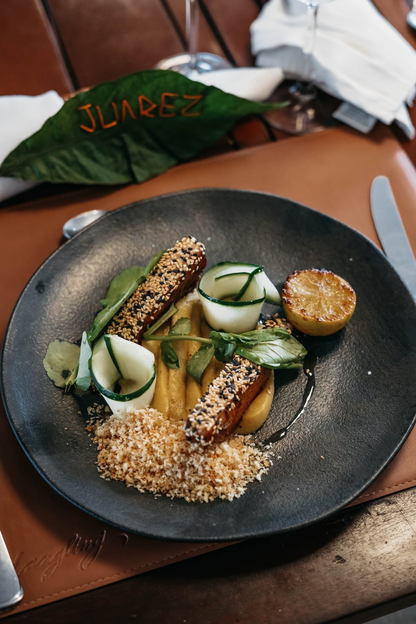 Sesambrust, Gurkenspirale, karamellisierte Zitrone. Jemand in der Küche weiß, was er tut. Mit Sesam panierte Proteinstreifen auf goldgelbem Püree, Gurkenschnecken, gerösteten Semmelbröseln und einer angekohlten Zitronenhälfte auf einem dunklen Teller im Restaurant Juarez, an Bord einer Luxus-Amazonas-Kreuzfahrt in Brasilien
