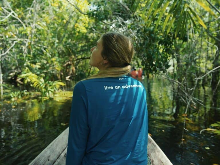 Reisende in einem Holzkanu blickt zum Blätterdach des überfluteten Regenwaldes bei einem Amazonas-Abenteuer