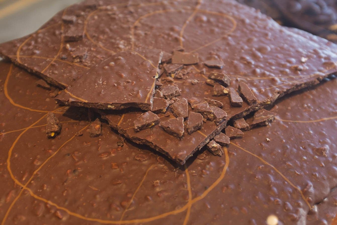 Van boon tot reep — met de hand gemaakt chocolade in het cacaohart van Bahia. Vers gebroken plakken ambachtelijke melkchocolade met nootjes op een marmeren oppervlak tijdens een bezoek aan een cacaoboerderij op de fietsroute door Bahia