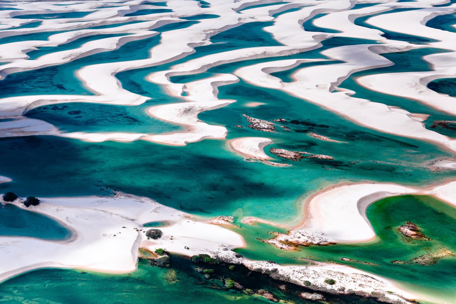 A mosaic of white and turquoise, sculpted fresh by the last rains. Photo: cokada Aerial view of the lencois maranhenses trek landscape, showing sweeping white sand dunes interlaced with vivid turquoise freshwater lagoons stretching to the horizon