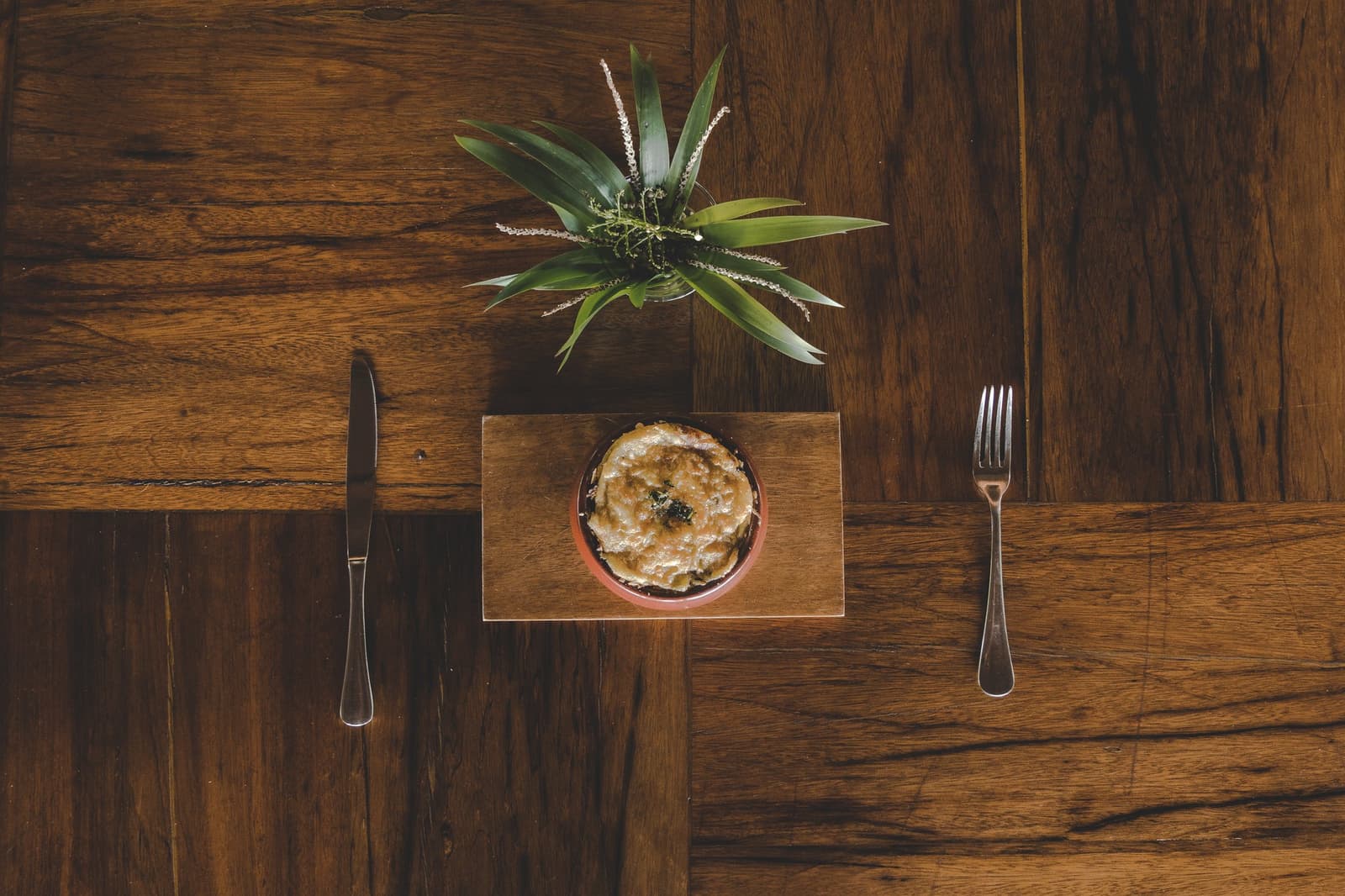 Au cœur de l'Amazonie, même le déjeuner prend son temps. Vue de dessus d'un plat gratiné dans un ramequin en terre cuite posé sur une planche en bois avec couteau et fourchette, dans le cadre d'un lodge de luxe en Amazonie brésilienne
