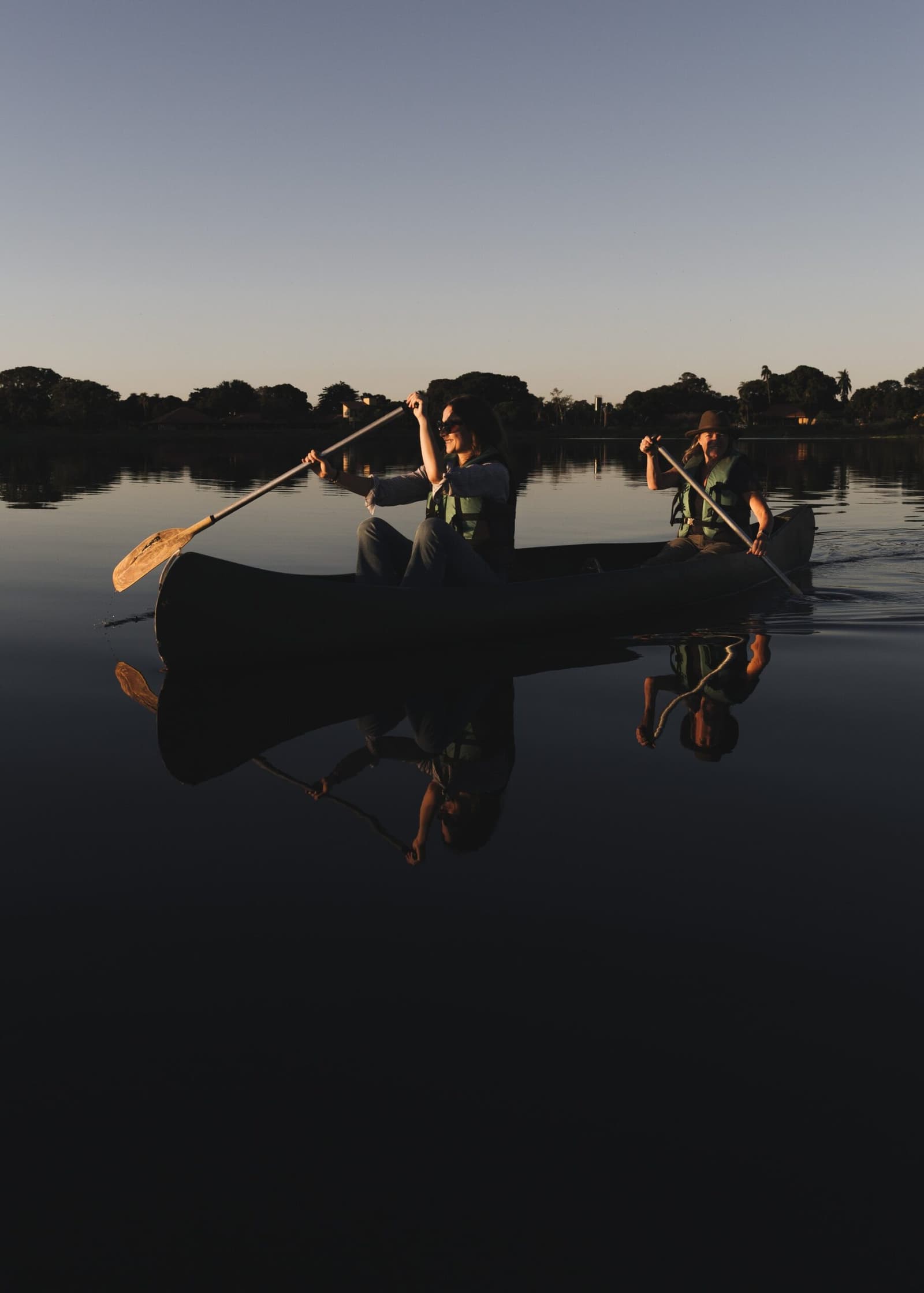 Perfectly still water, two paddles, and a fading sky — some evenings simply refuse to be rushed. Two guests in life vests paddle a canoe across mirror-still water at dusk on a pantanal luxury safari, their reflections perfectly mirrored on the glassy surface