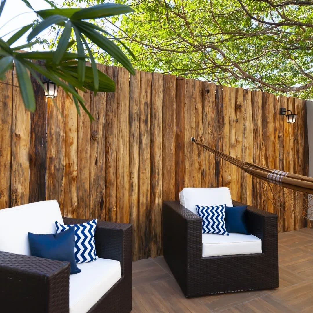 Rattansessel, eine Hängematte und Baumschatten — die perfekte Pause zwischen zwei Wildtiertouren. Überdachte Terrasse einer Lodge auf der Pantanal-Tour ab Cuiabá mit Rattansesseln, weißen Kissen, blau-weißen Zierkissen, einer Hängematte und rustikalen Holzwänden unter grünem Blätterdach
