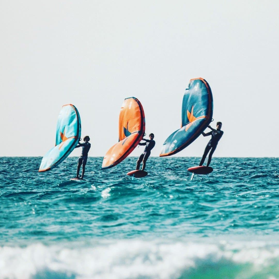 Three riders, three wings, one endless blue — wing foiling at its most electric. Photo 2