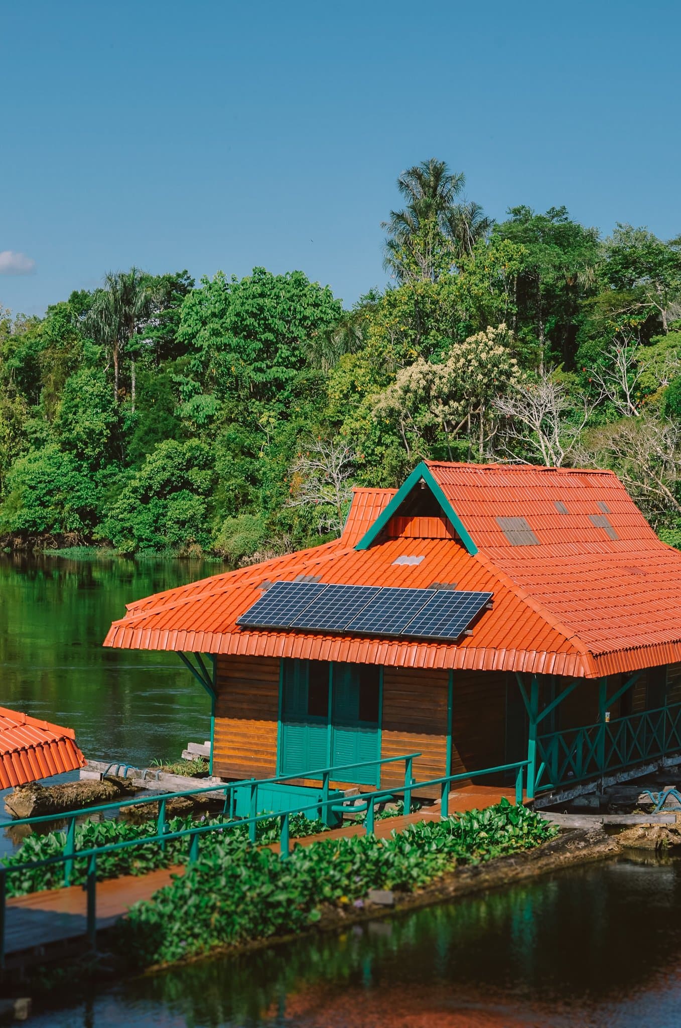 Stroom van het dak, bos aan alle kanten. Zo ziet een goede uitvalsbasis eruit. Drijvende houten hut met oranje pannendak en zonnepaneel op een donkere rivier, omringd door dicht tropisch regenwoud — onderdeel van een amazon rainforest ecolodge trip in brazil bij de Uakari Lodge