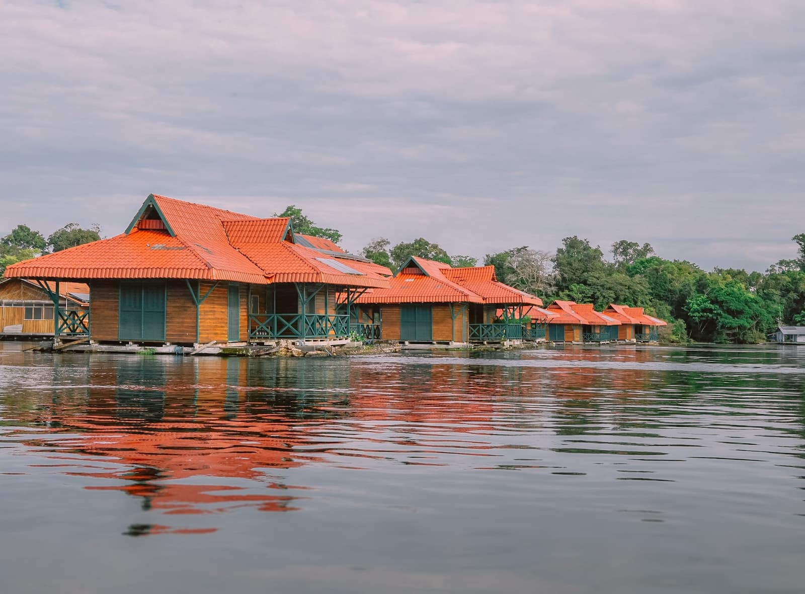 Rode daken op het water, oerwoud op een steenworp afstand. Een rij houten hutten met terracottakleurige pannendaken drijft op een kalme rivier bij de Uakari floating lodge, hun oranje spiegelingen golven over het water met dicht bos op de achtergrond