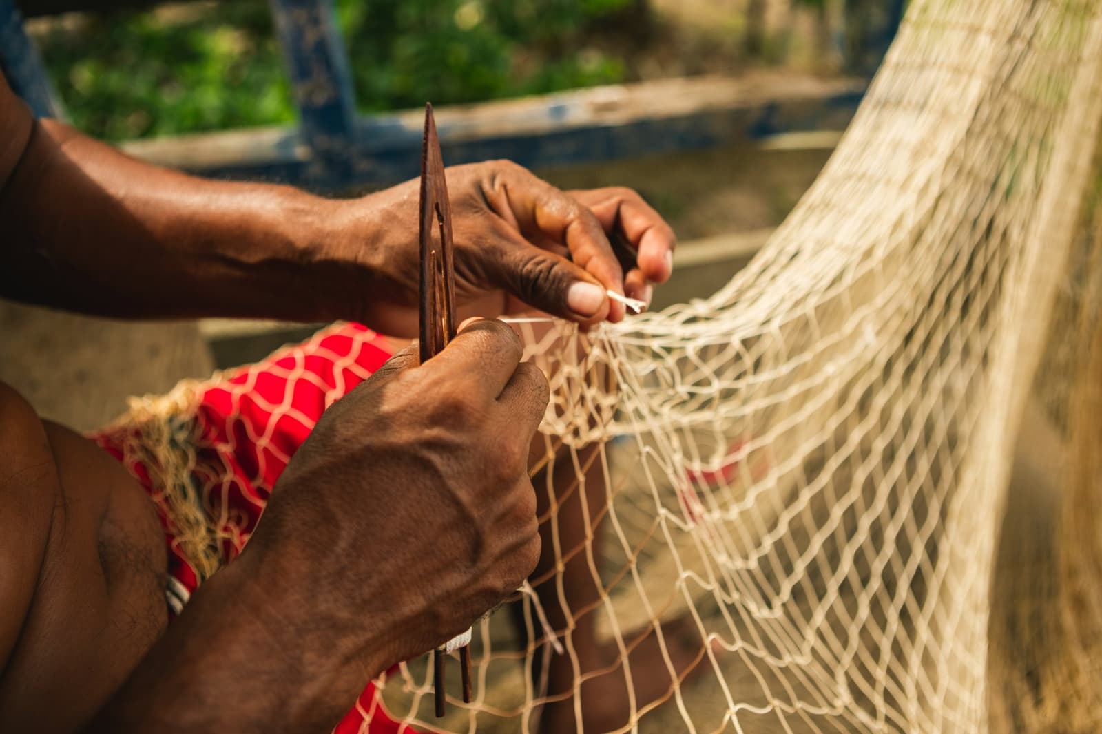 Knoop voor knoop, vakmanschap dat de rivier zijn gang geeft. Photo: Guilherme Gomes Close-up van handen die met een houten naald een visnet herstellen tijdens een bezoek aan een riviergemeenschap op een amazone regenwoud ecolodge reis in brazilië